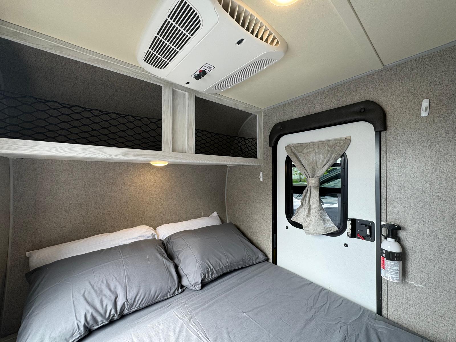 Cozy RV rental bedroom with a comfortable bed, overhead storage, AC unit, and a fire extinguisher for safety.. Forest River Rockwood Geo Pro 2018
