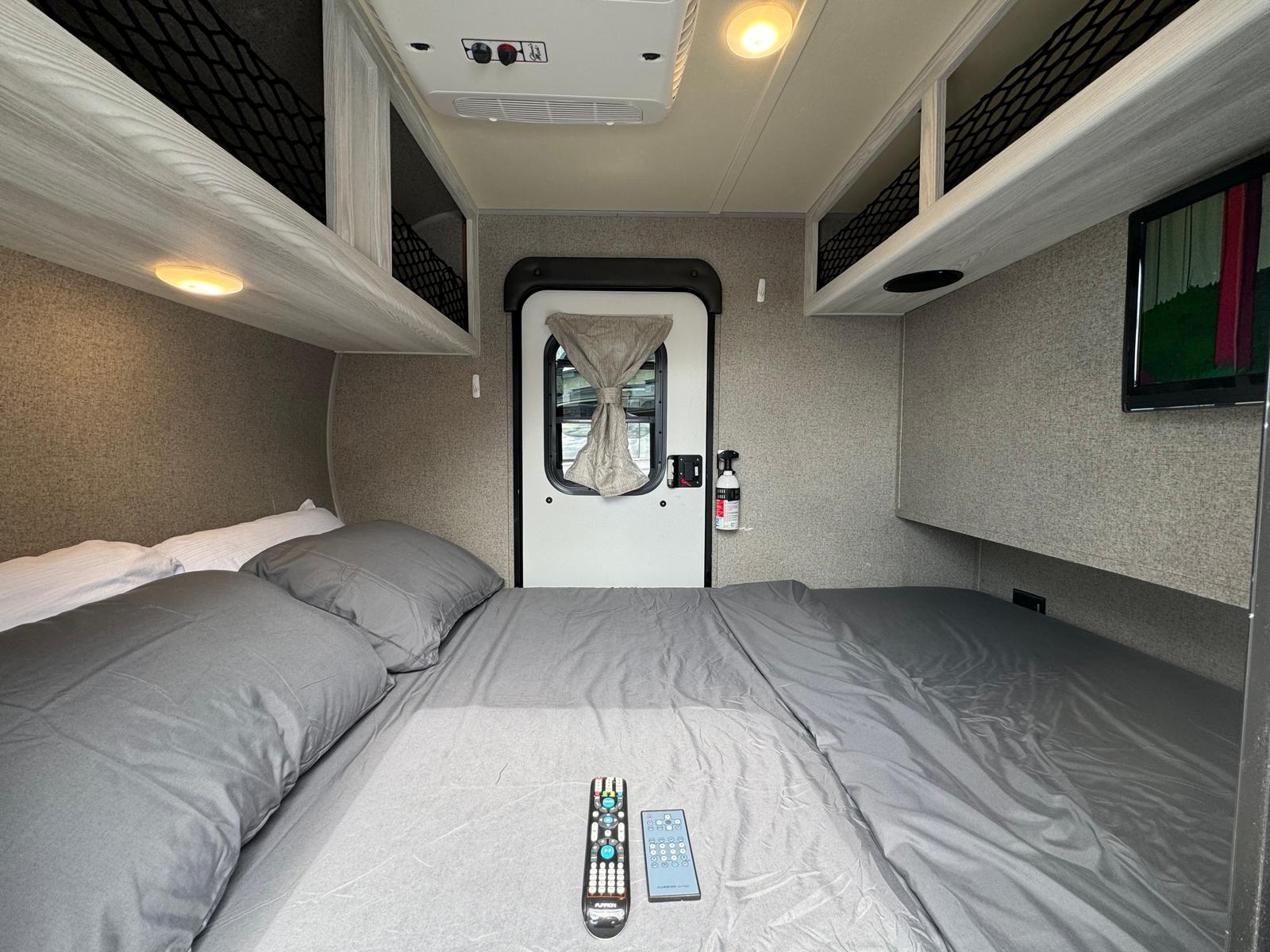 Inside this RV rental: a comfy bed with remotes, TV, AC, overhead storage, and emergency fire extinguisher.. Forest River Rockwood Geo Pro 2018