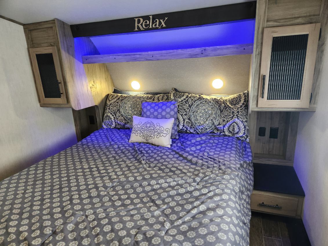 Cozy RV rental bedroom with 'Relax' sign, blue under-shelf lighting, patterned bed, and bedside storage.. Forest River Cherokee Arctic Wolf 2022