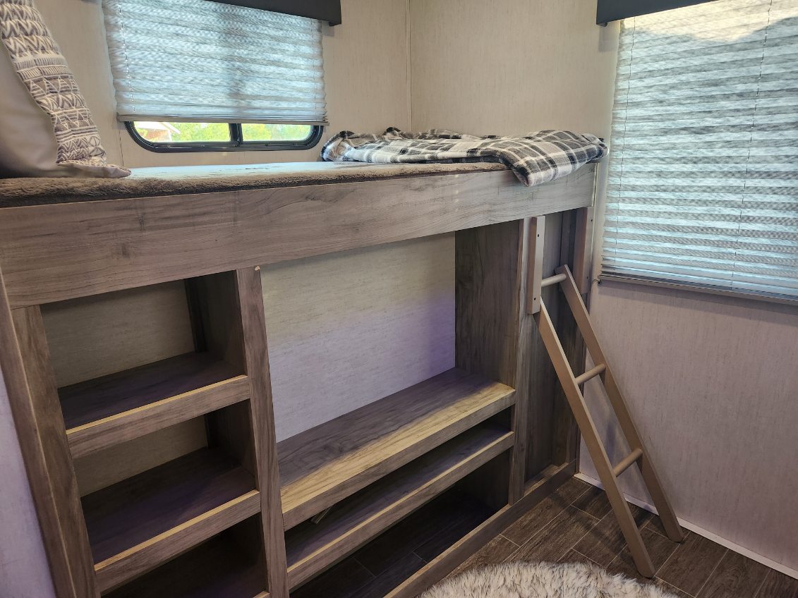 Cozy RV rental bunk beds with storage, a window, and plaid blanket. Features a wooden ladder for access.. Forest River Cherokee Arctic Wolf 2022