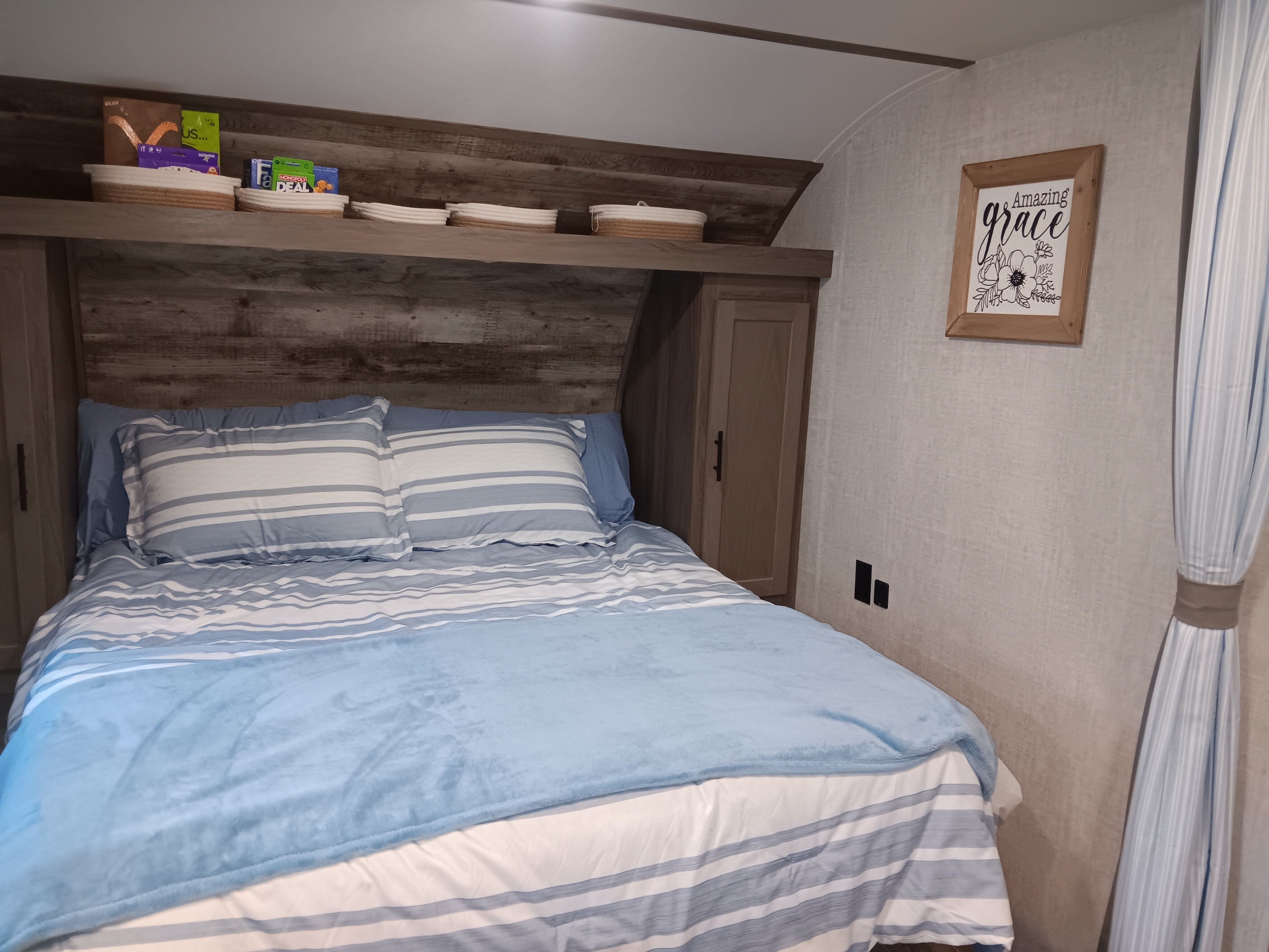 Cozy RV rental bedroom features blue striped bedding, overhead storage, and an 'Amazing Grace' sign.. Gulf Stream 762t248bh7787 2022