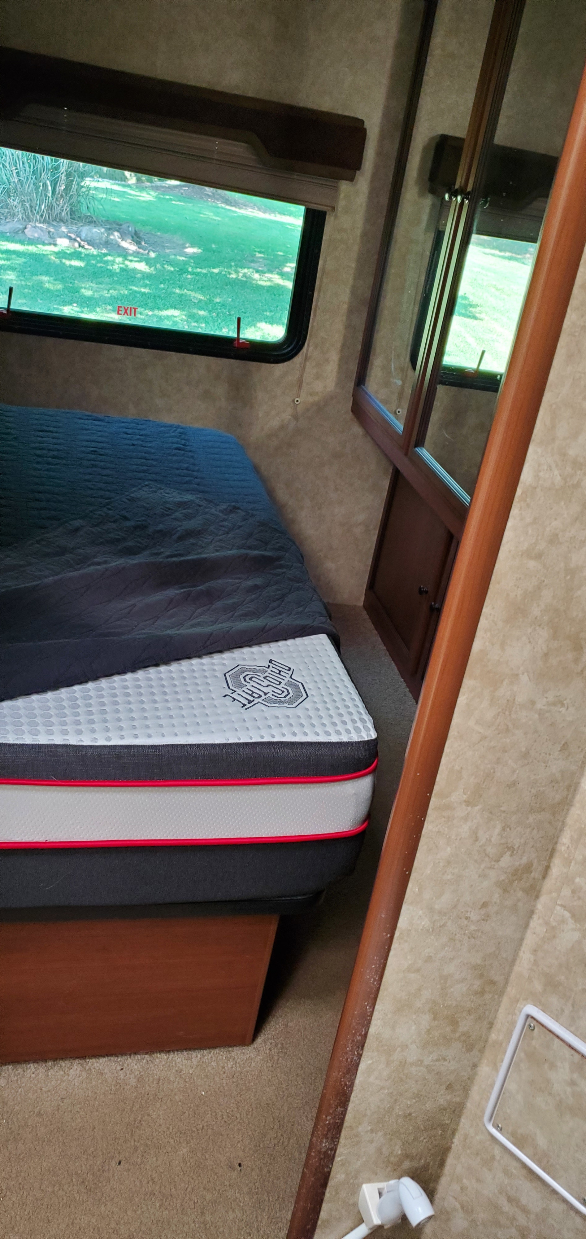 Cozy RV rental bedroom featuring an Ohio State mattress, an emergency exit window overlooking green outdoors, and a wall mirror.. Jamboree Sport 2013