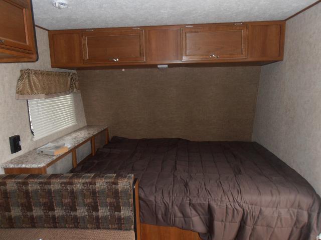 View of an RV rental's bedroom, showing a large bed with a brown comforter, wooden overhead cabinets, and a window.. Avenger Avenger Trailer 2016
