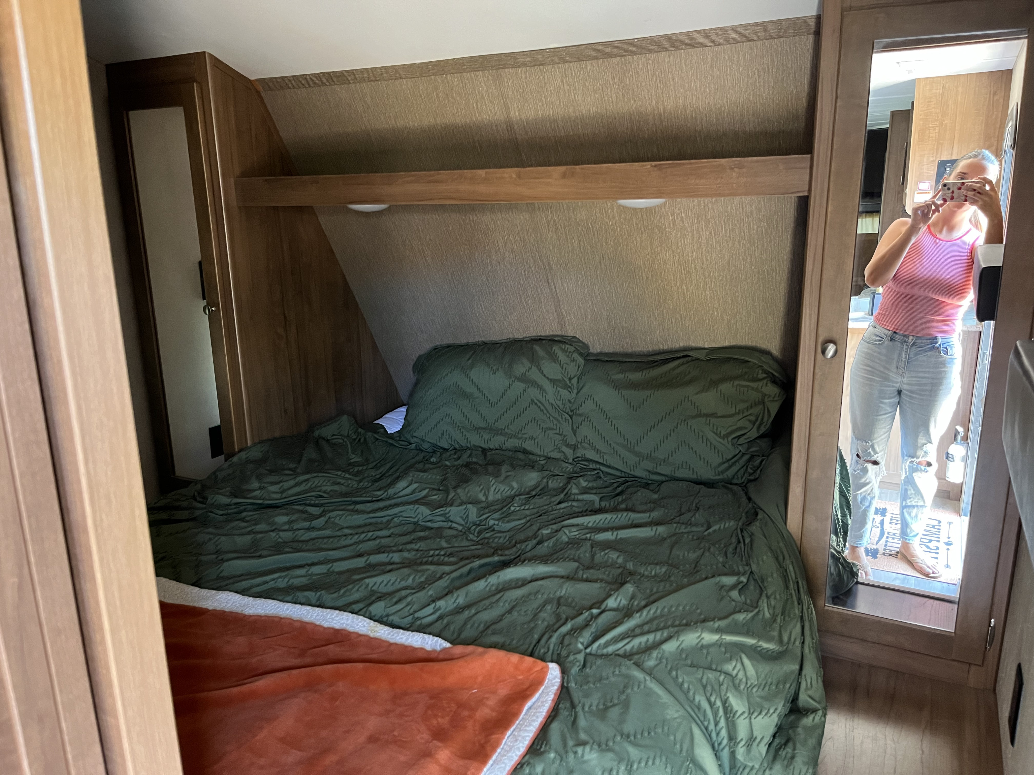 Cozy RV rental bedroom with dark green bedding and wooden built-ins. A mirror reflects the person taking the photo.. Aspen Trail Aspen Trail Trailer 2018