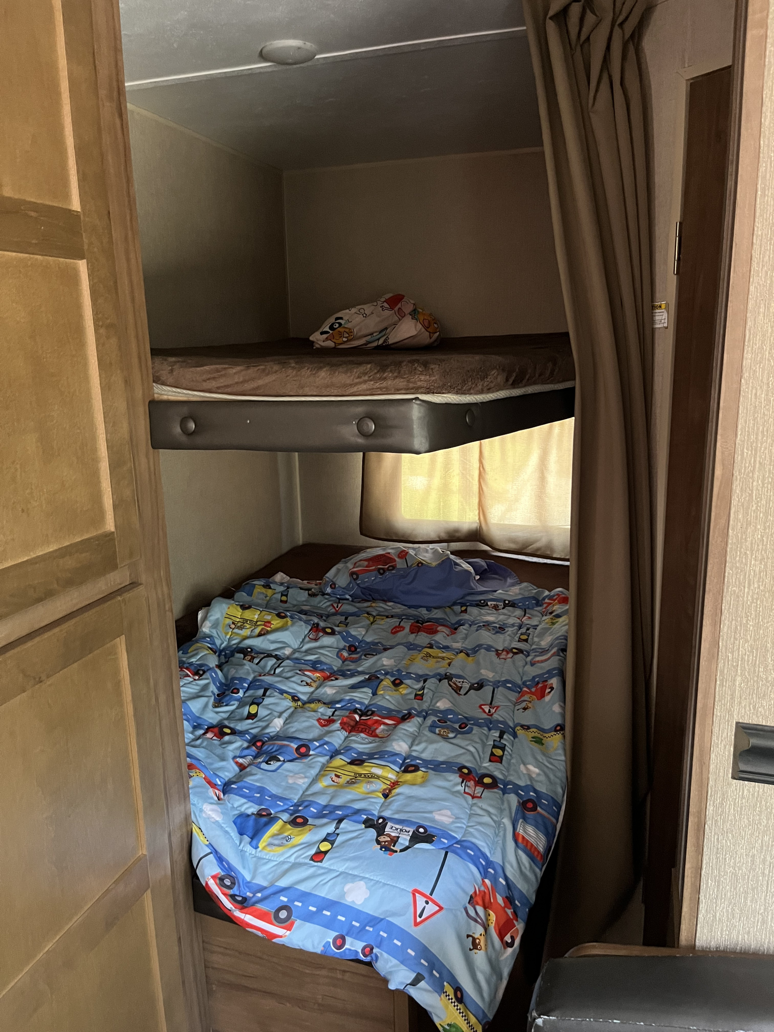 Inside an RV rental: a small bunk bed sleeping area with a colorful vehicle-themed comforter on the bottom bunk.. Aspen Trail Aspen Trail Trailer 2018