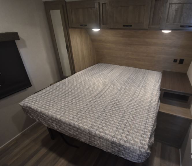 Comfortable RV rental bedroom featuring a bed with patterned cover, overhead cabinets, and a nightstand.. Forest River Vibe 2020