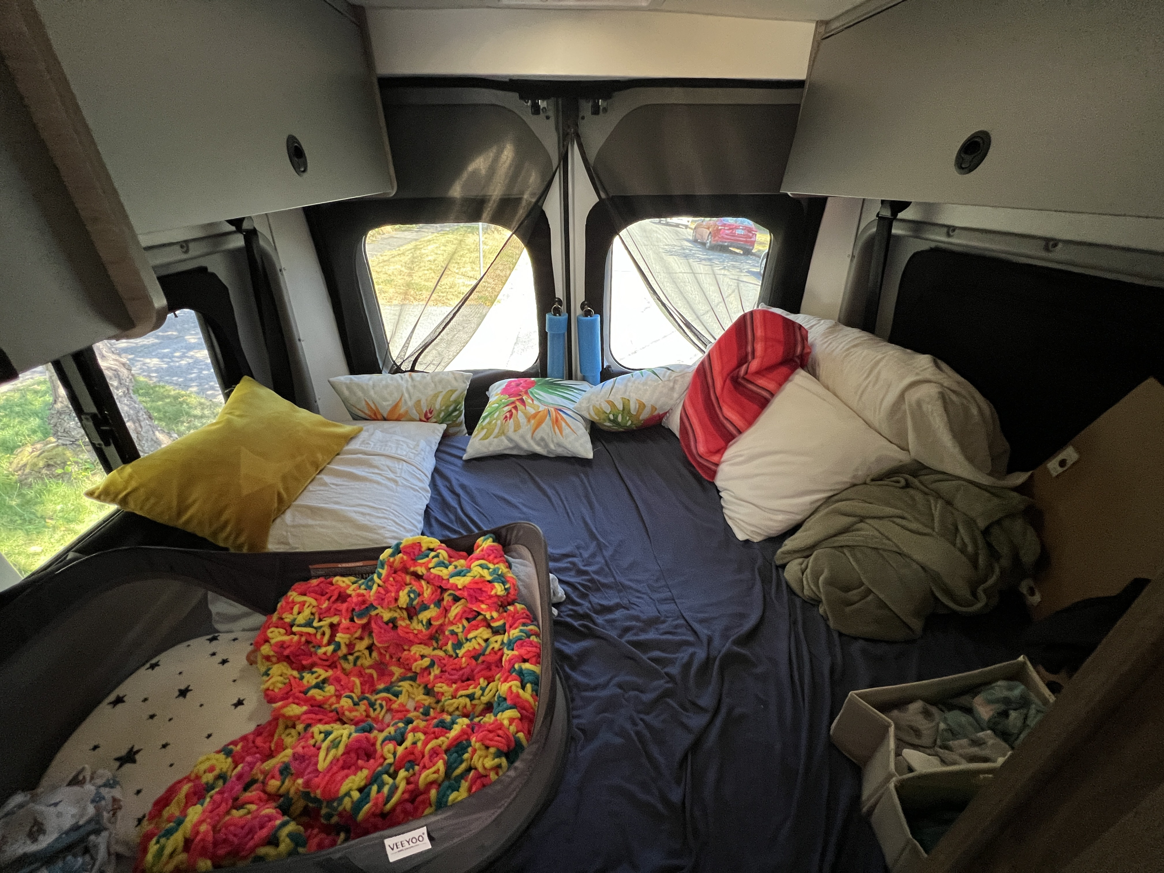 Cozy RV rental interior with a spacious bed, baby bassinet, and storage, perfect for family travel.. Winnebago Solis 2021