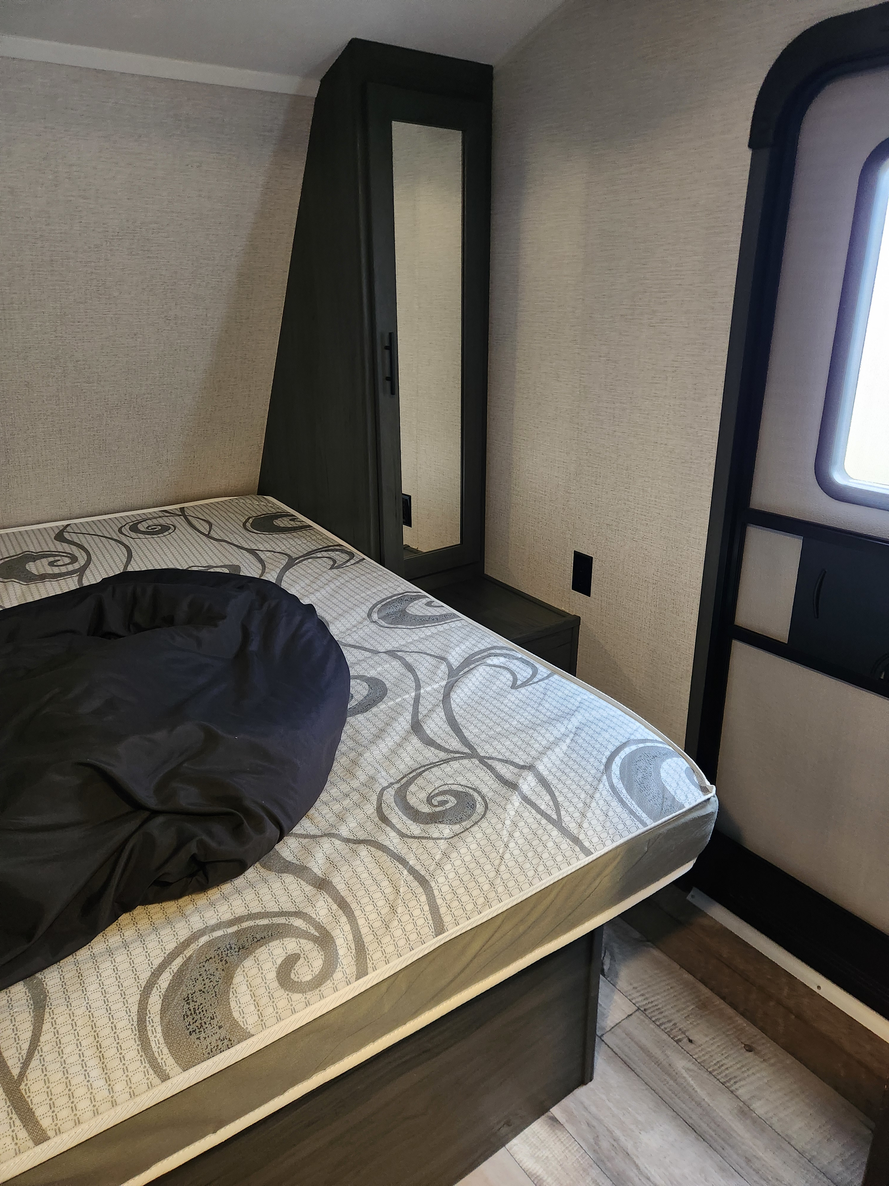RV rental bedroom: a bed with patterned mattress, mirrored cabinet, and exit door with window on textured walls.. Dutchmen Aspen trail 29bb 2021