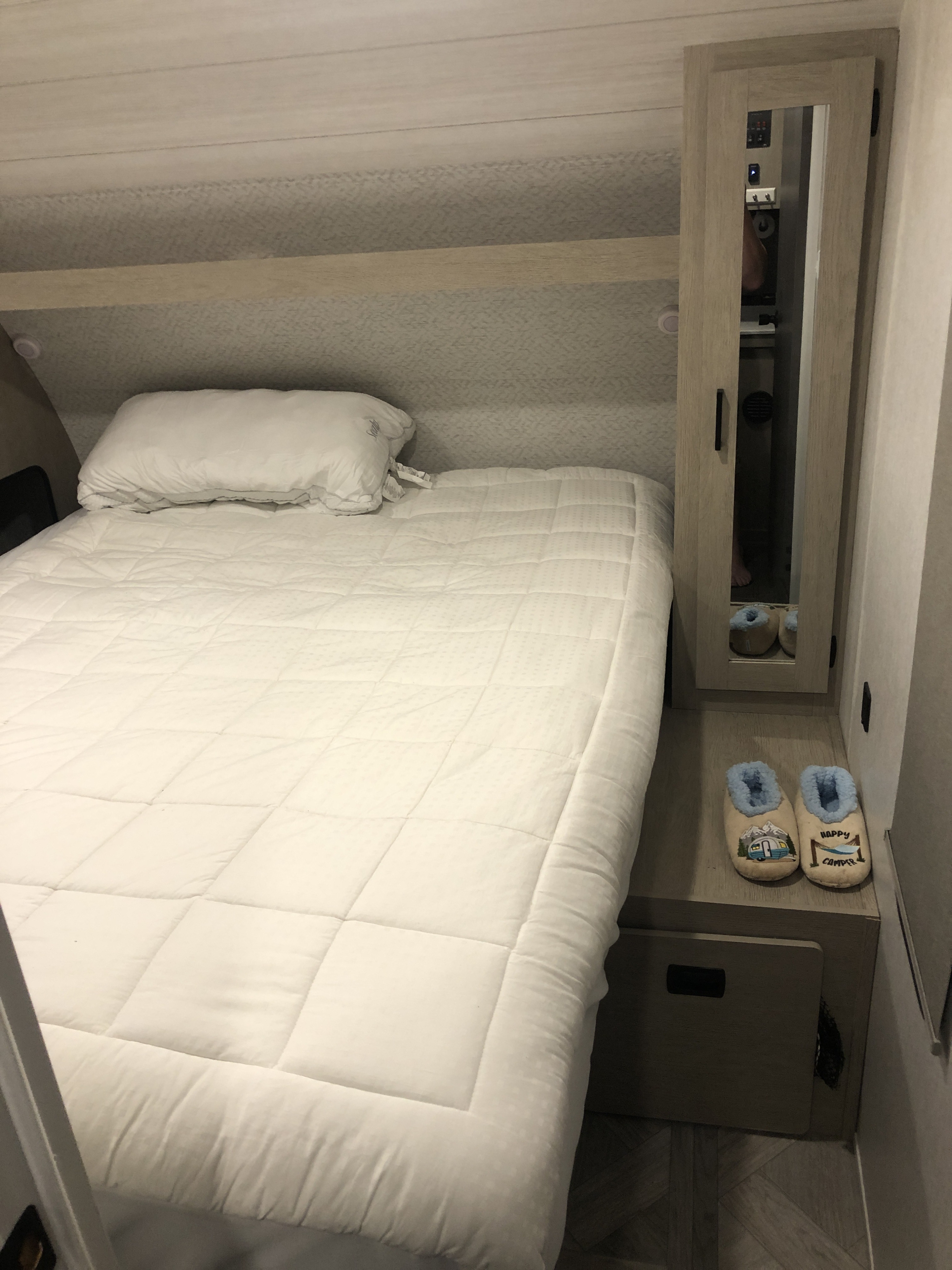 Cozy RV rental bedroom with white bed, pillow, and "Happy Camper" slippers. Perfect for a relaxing trip!. Forest River Salem Cruise Lite Platinum 2023