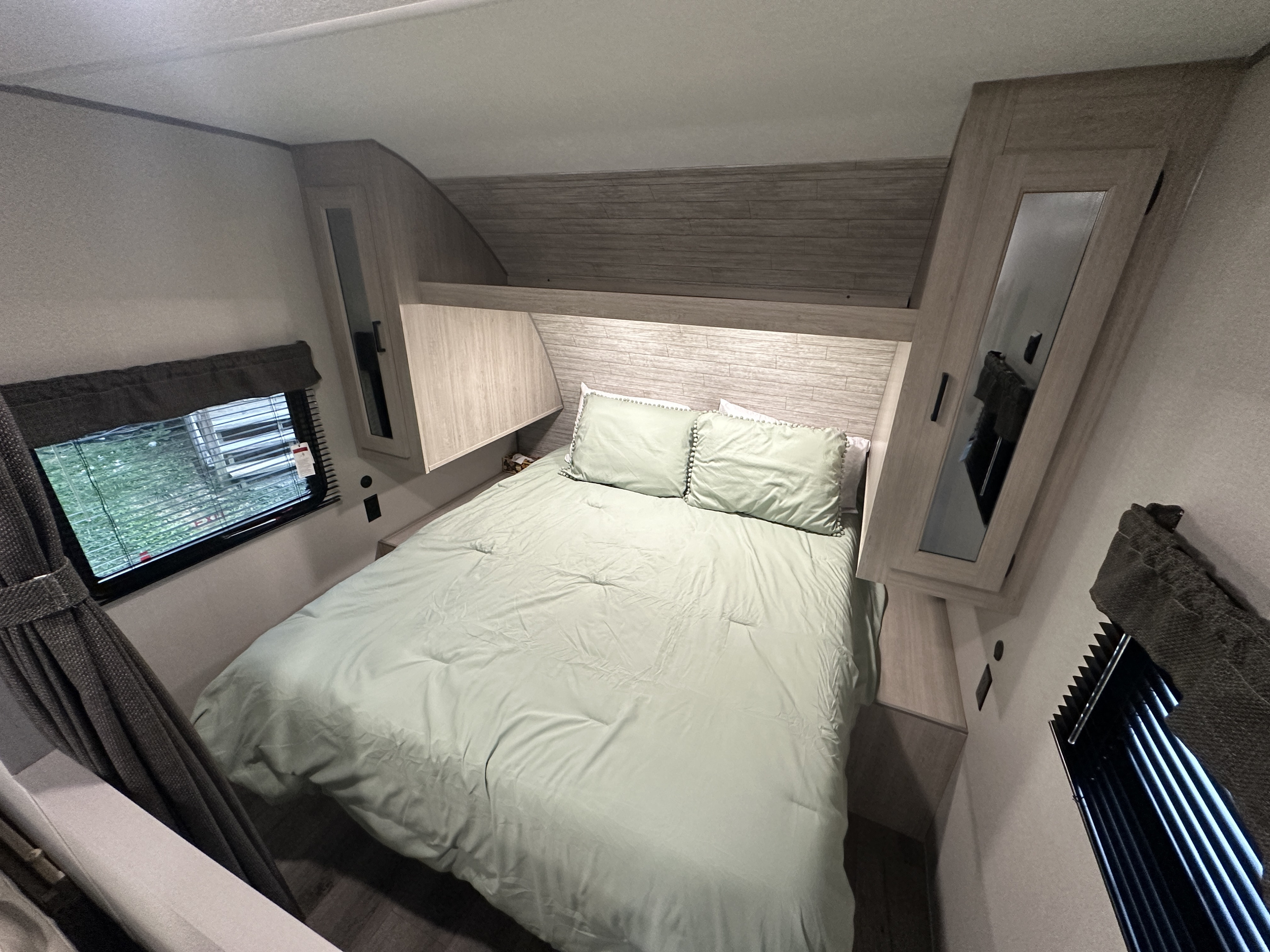 RV rental bedroom with a light green bed, integrated wood-look storage cabinets, and a window. A comfortable and modern RV interior for your trip.. Coachmen 261BH 2024