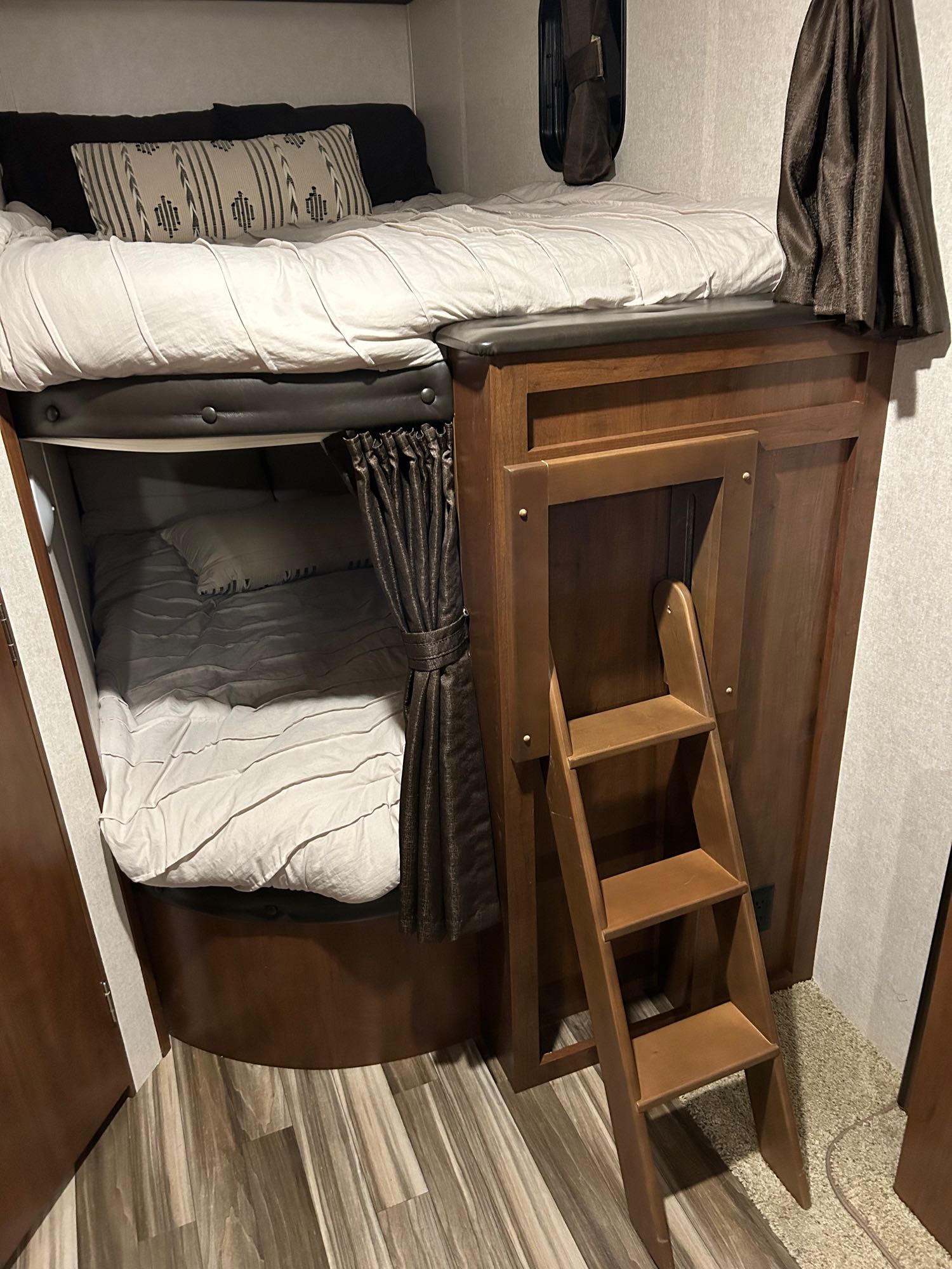 An RV rental's interior shows a set of bunk beds with a ladder. The top bed is made; the bottom has a privacy curtain.. Jayco Jay Flight SLX 2017