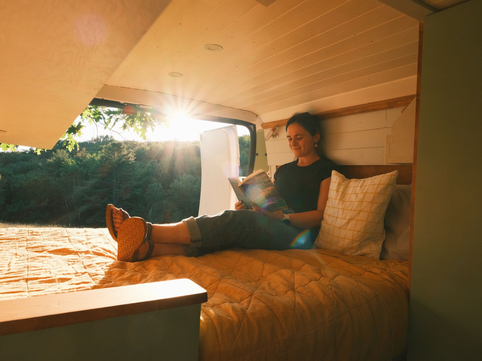 A woman reading in a sunlit RV rental, serene nature view outside. Perfect cozy escape.. Other Other 2018