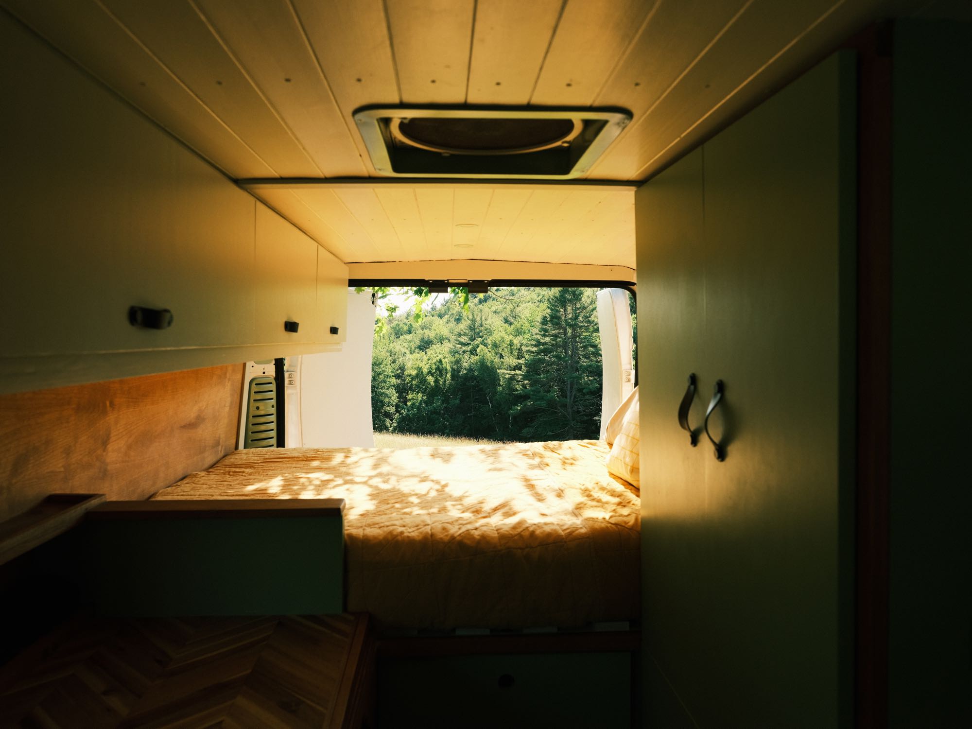 Cozy RV rental van interior: a bed with a forest view, wood paneling, and cabinets.. Other Other 2018