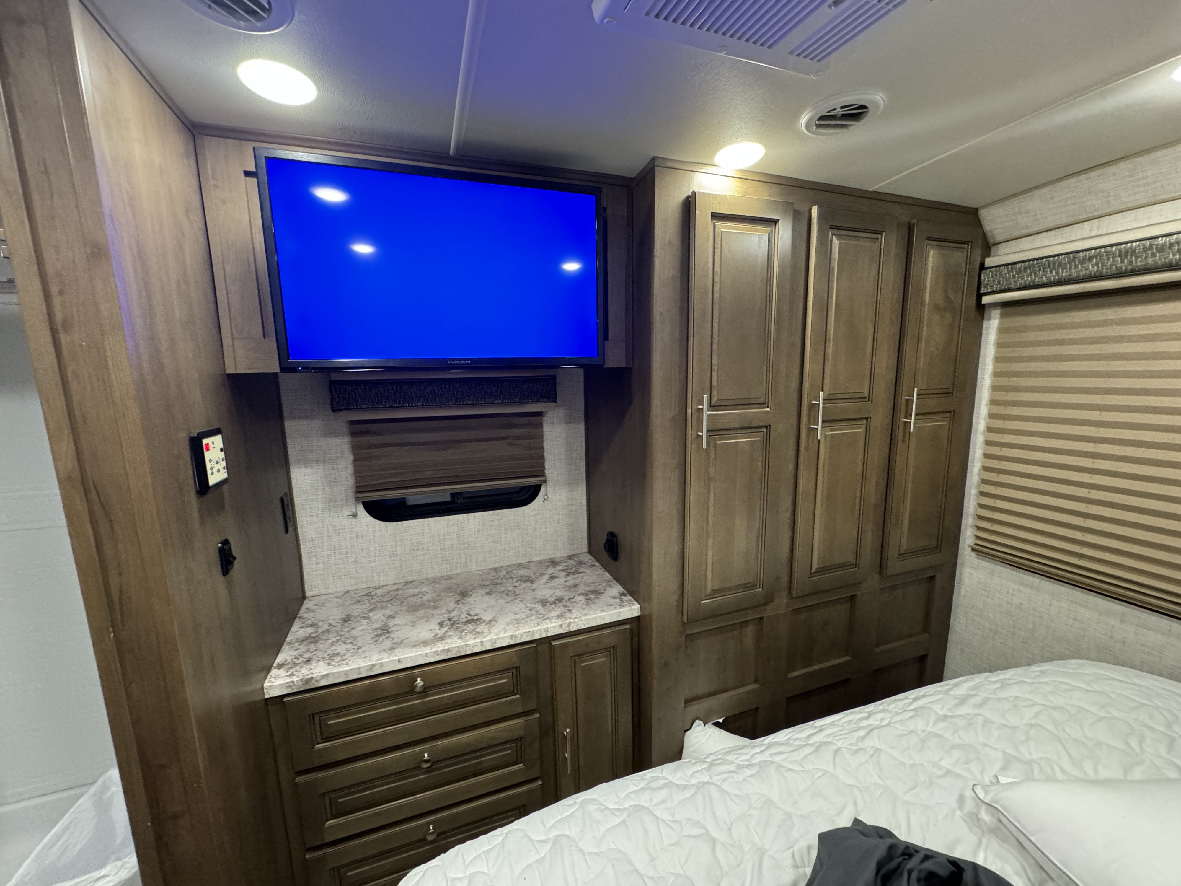 An RV rental bedroom interior with a TV, dark wood cabinets, countertop, and a white-quilted bed, showing a compact living space.. Forest River Georgetown 2019