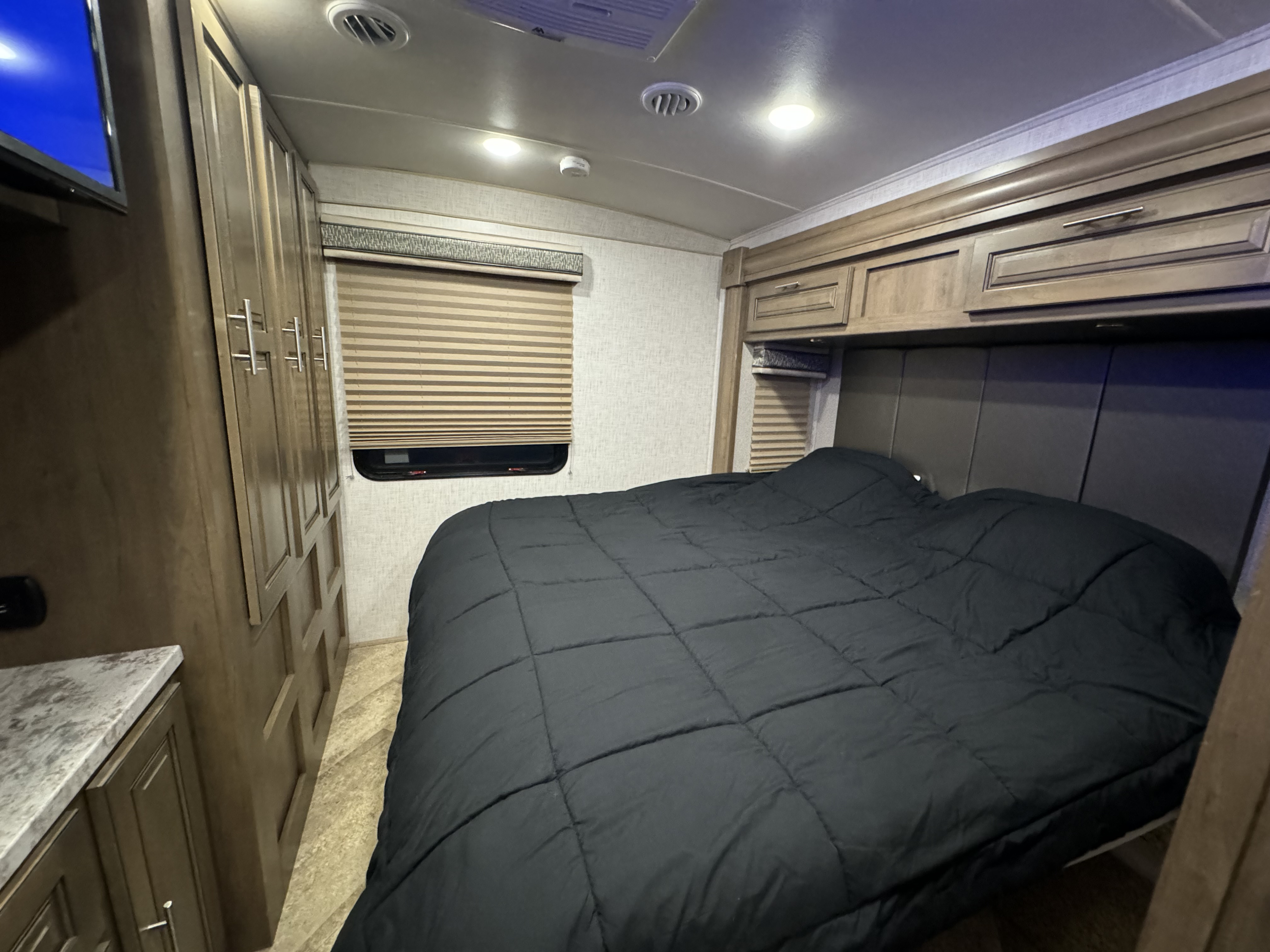 Spacious RV rental bedroom showcasing a comfortable bed, ample storage cabinets, and a window with blinds.. Forest River Georgetown 2019