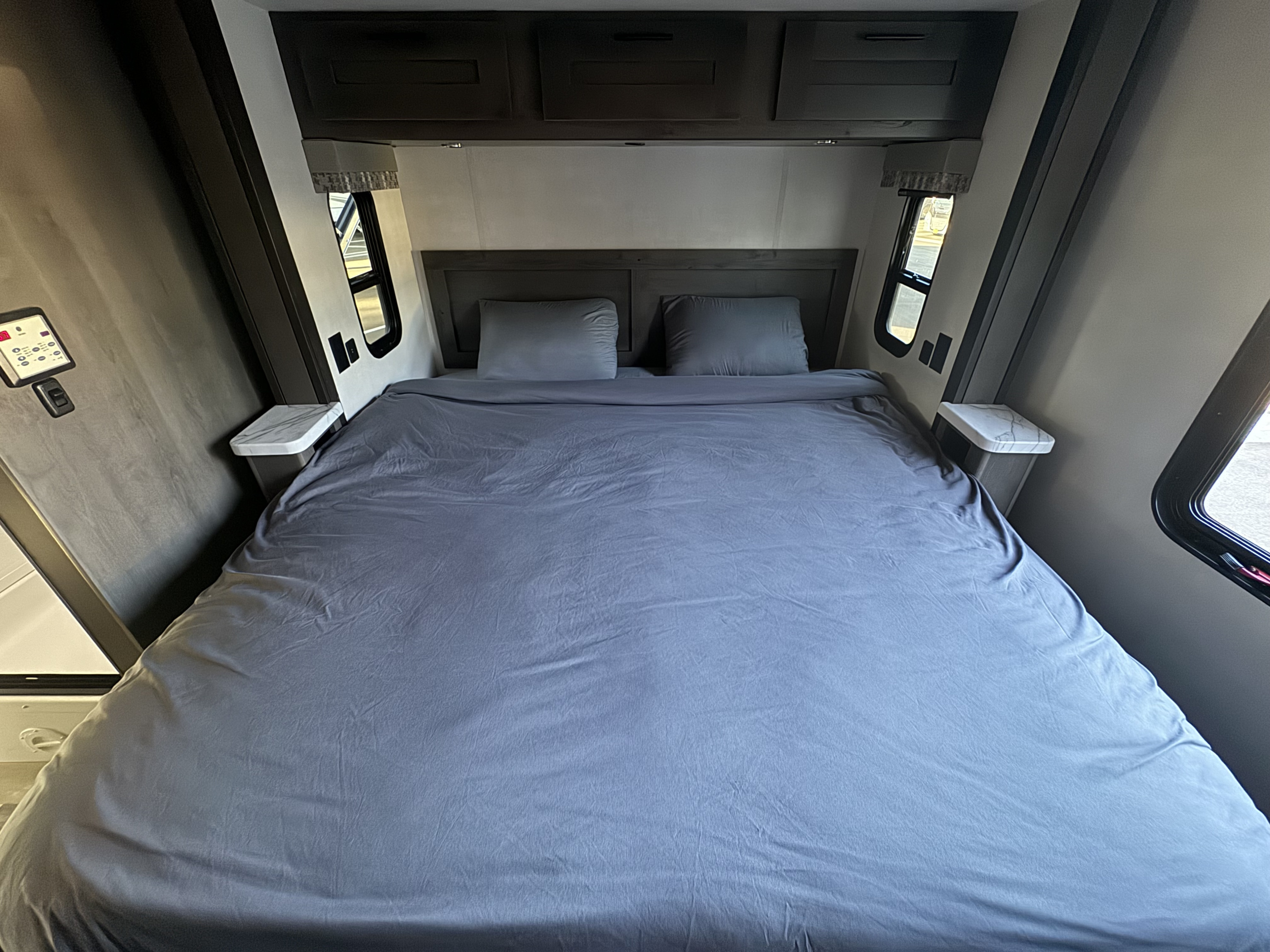 Clean and cozy RV rental bedroom featuring a queen bed with gray linens, overhead cabinets, and side windows.. Forest River Fr3 2021