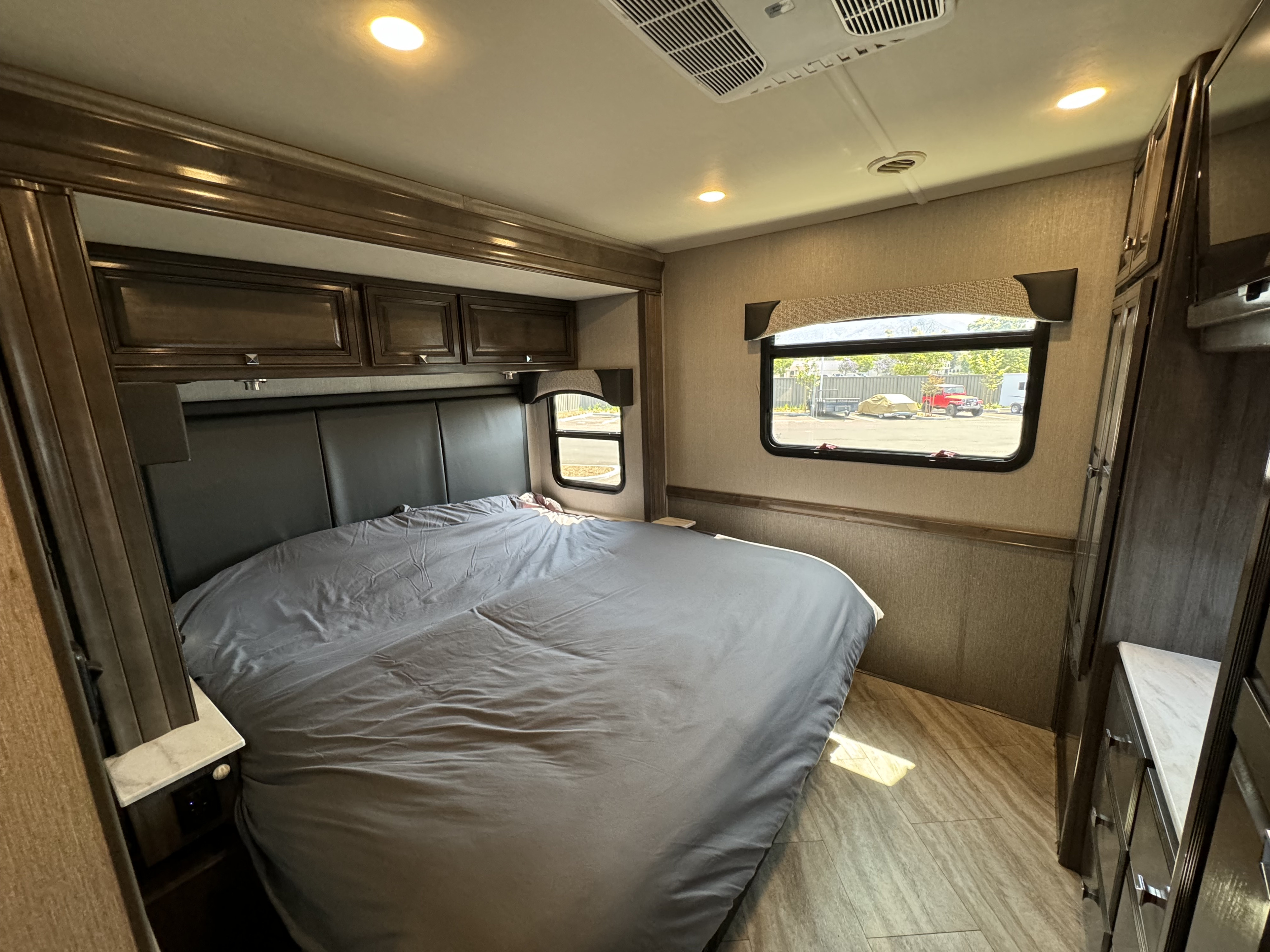 RV rental bedroom interior with a comfortable bed, overhead cabinets, and window views. Ideal for a relaxing trip.. Fleetwood Fortis 2021