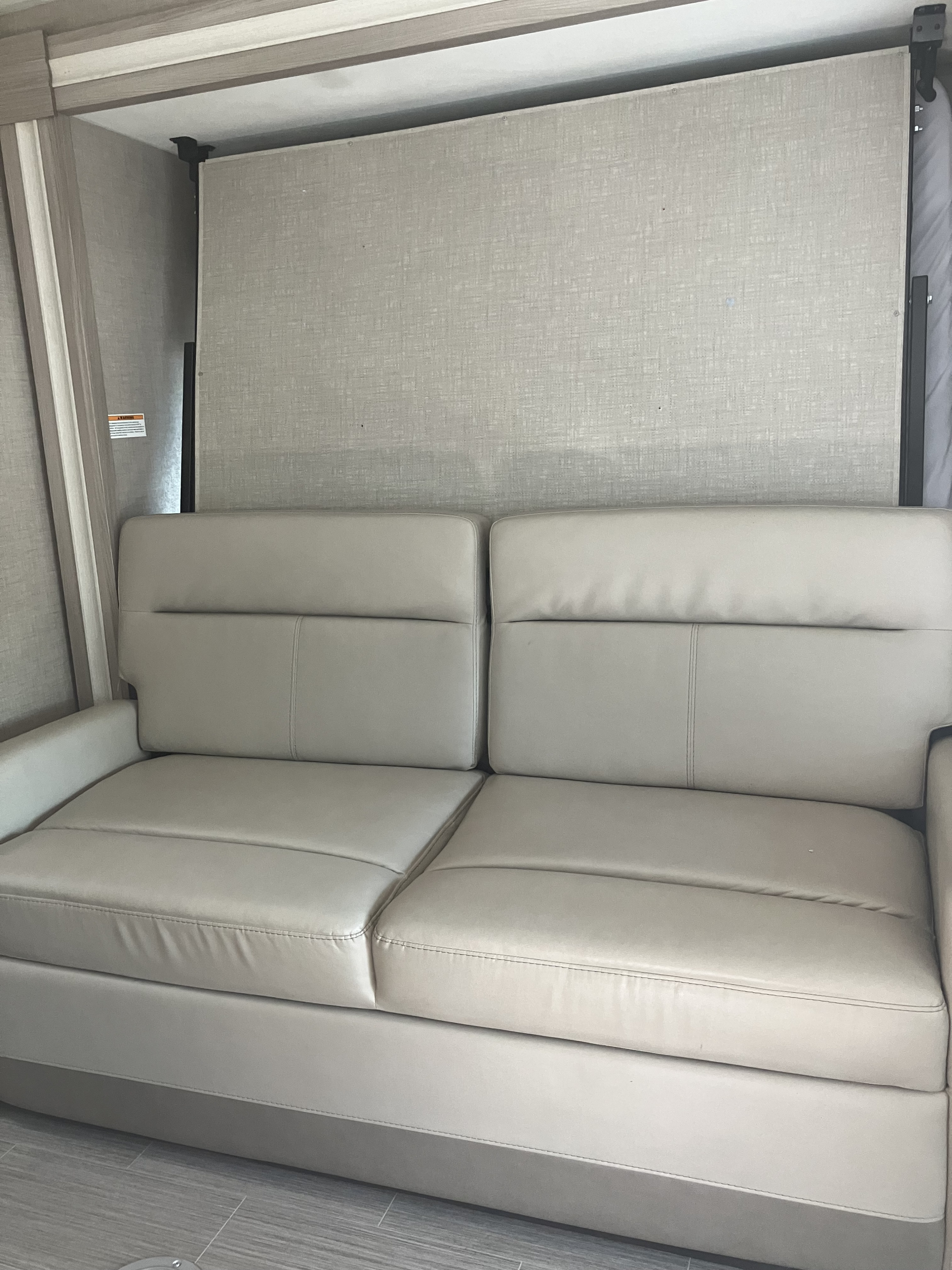 Modern RV rental interior with a light beige sofa and a textured wall panel, potentially a fold-down bed, for smart space utilization.. Thor Motor Coach Compass 2022