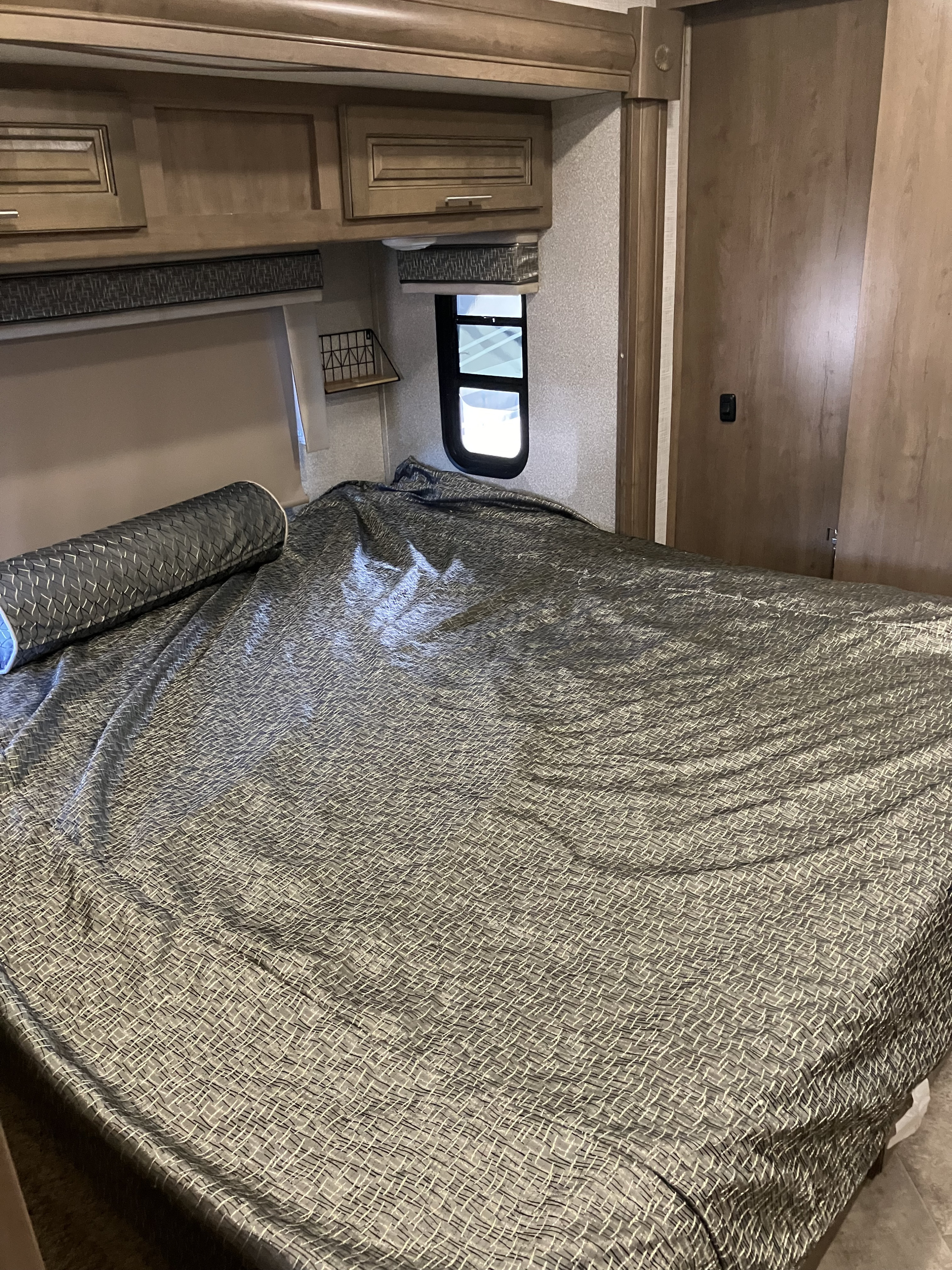 An RV rental bedroom showing a gray patterned bed, wooden overhead cabinets, and a side window.. Forest River GEORGETOWN GT5 2019