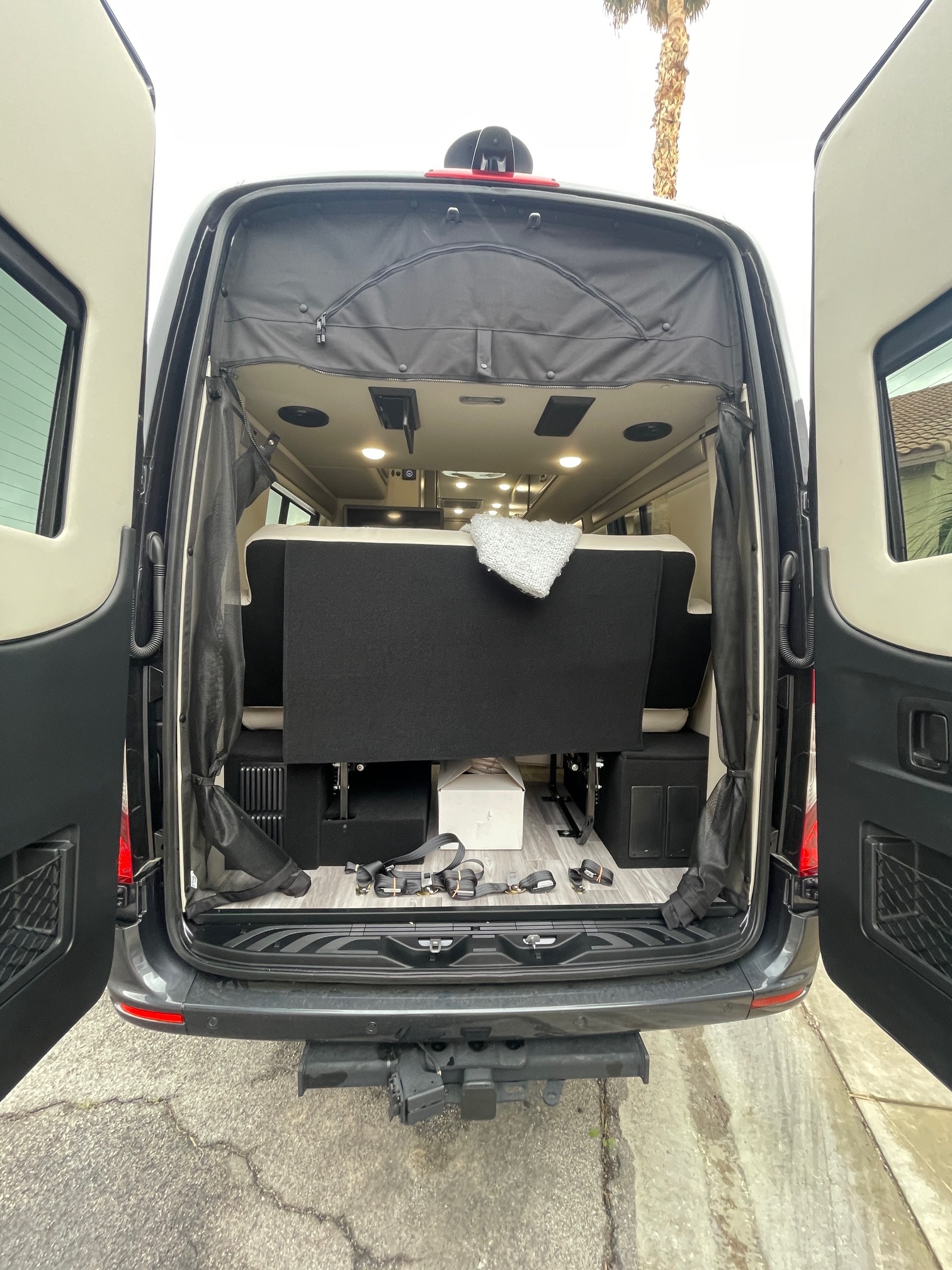 Open rear doors of an RV rental van reveal a functional interior with a convertible bench bed and side mesh screen.. Holiday Rambler Expedition 2024