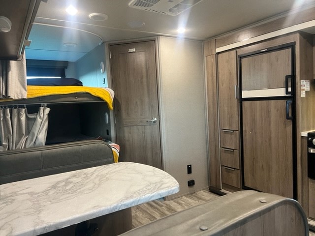 RV rental interior: comfy bunk beds, a dining table, and a fridge are visible, offering family comfort on the road.. Grand Design Imagine XLS 2021