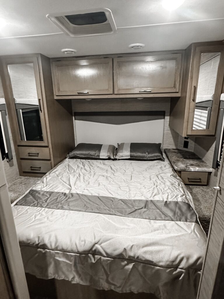Compact and modern RV rental bedroom featuring a bed, overhead cabinets, mirrored storage, and a skylight.. Thor Four Winds 2022