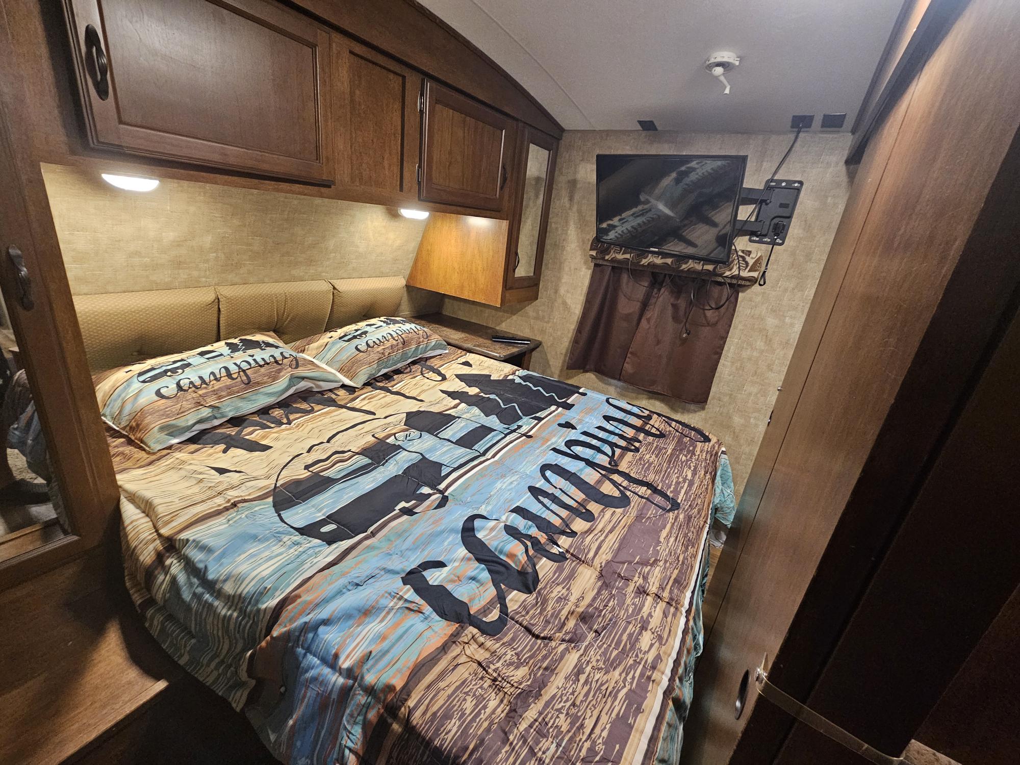 Cozy rv rental bedroom featuring a 'Camping' themed bed, overhead storage, and a mounted TV, ready for travel.. KZ Spree 301RIK 2015