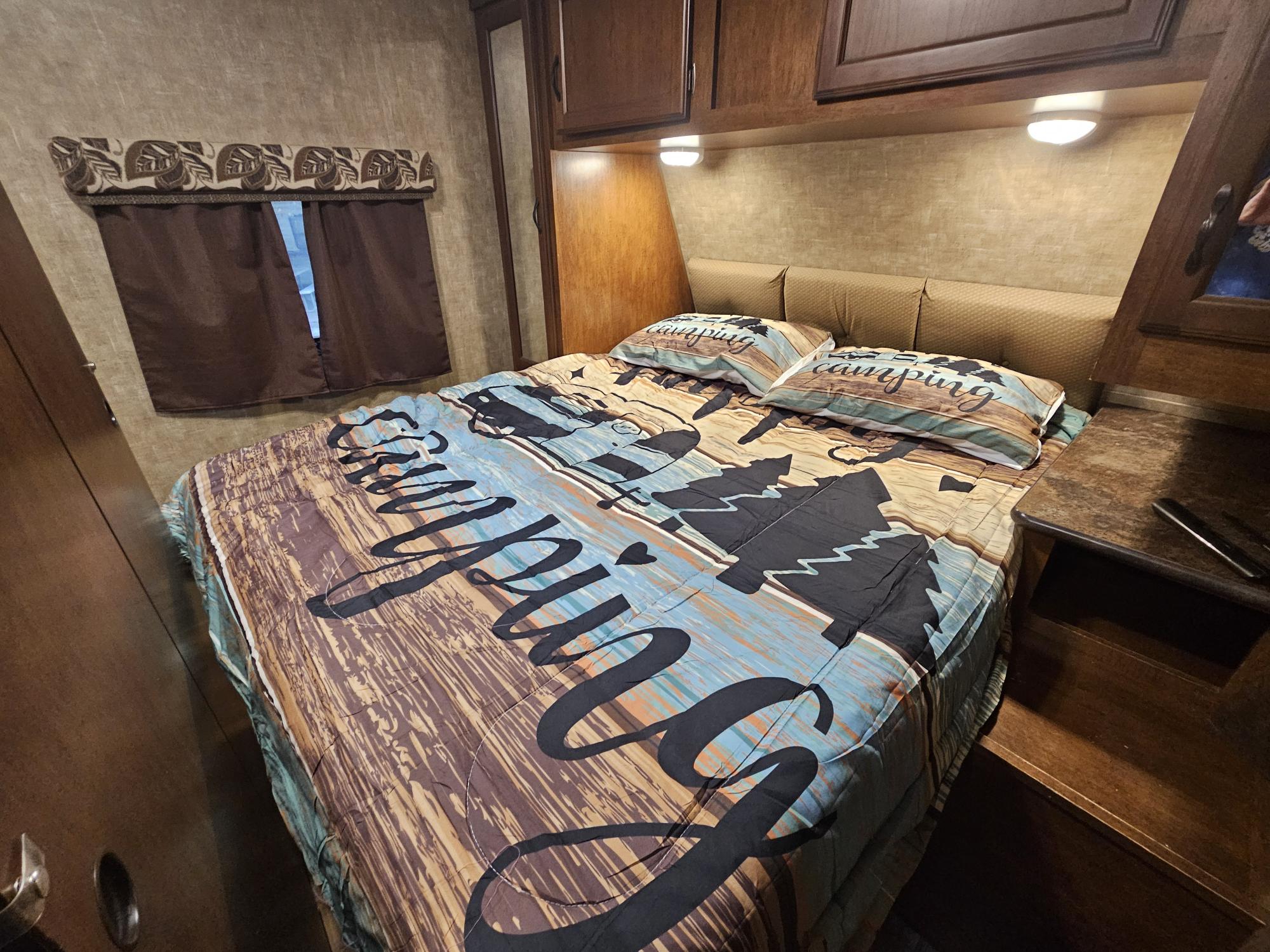RV rental bedroom: cozy bed with "Camping" themed bedding, wood cabinets, and a window.. KZ Spree 301RIK 2015