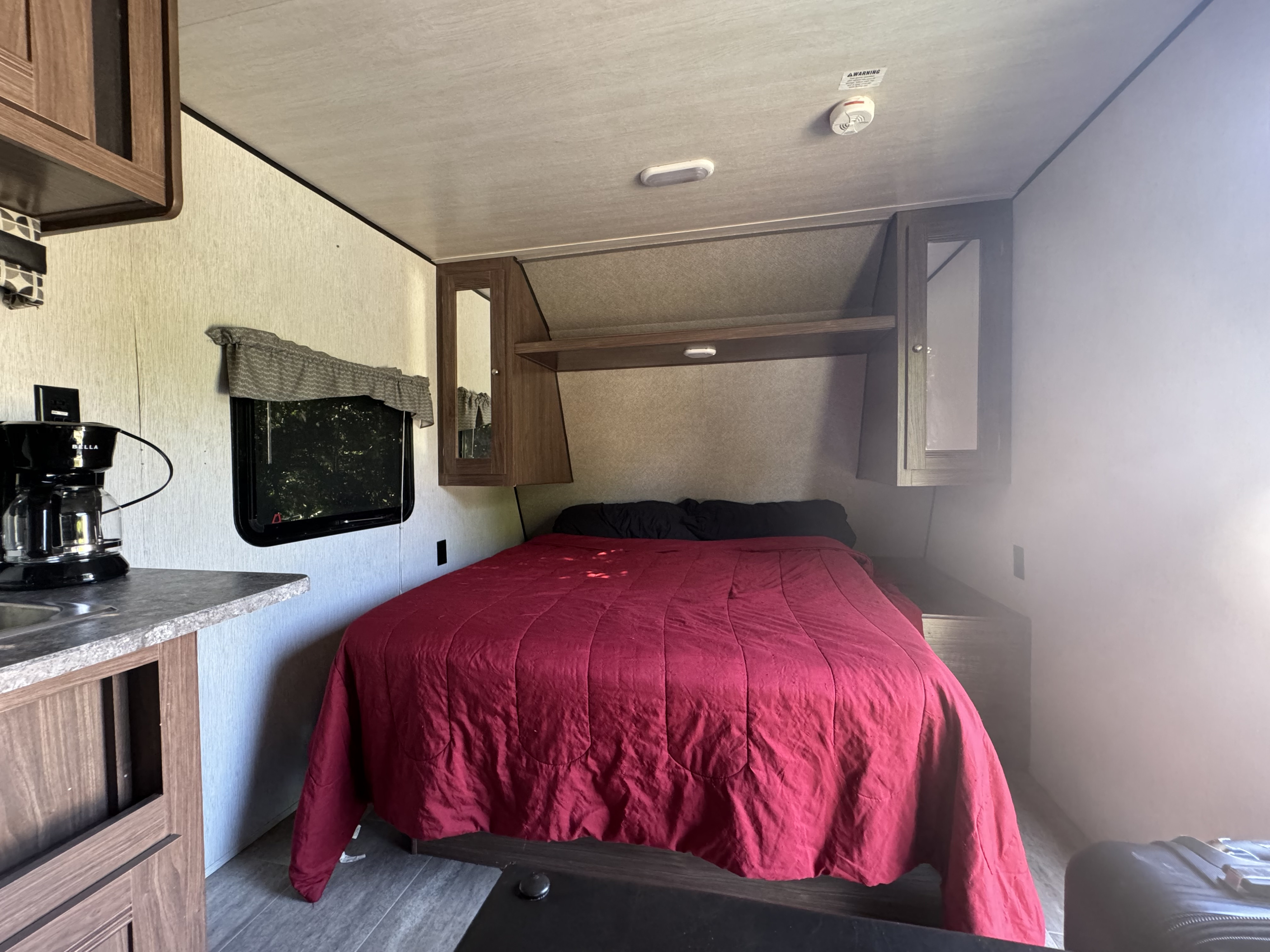 RV rental interior featuring a comfy bedroom with a red comforter, small kitchenette, and overhead storage.. Heartland RVs Trail Runner SLE 2019