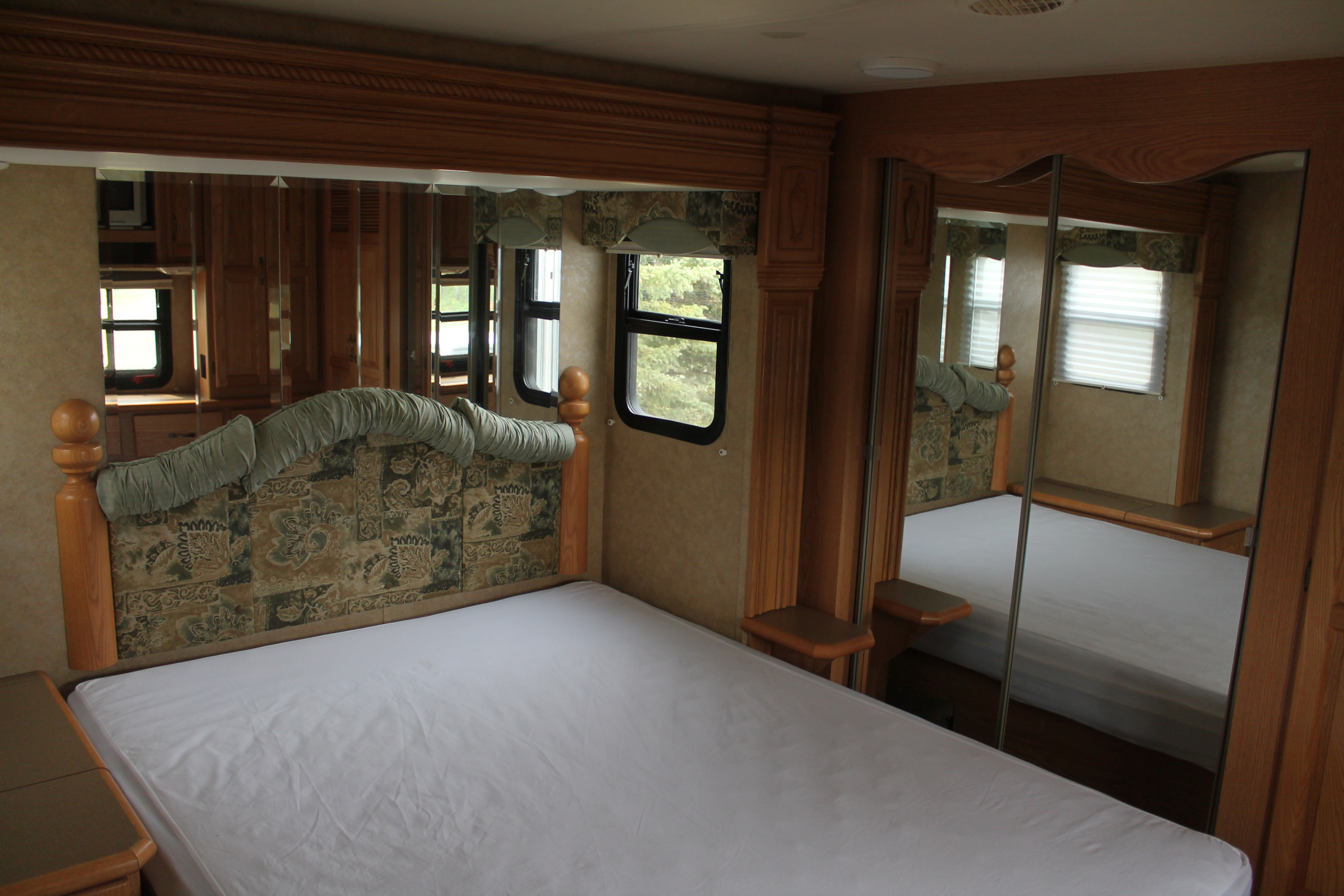 Spacious RV rental bedroom featuring a large bed, mirrored closet doors, and windows, designed for comfortable travel.. Newmar Cypress 33 RSLH 2007