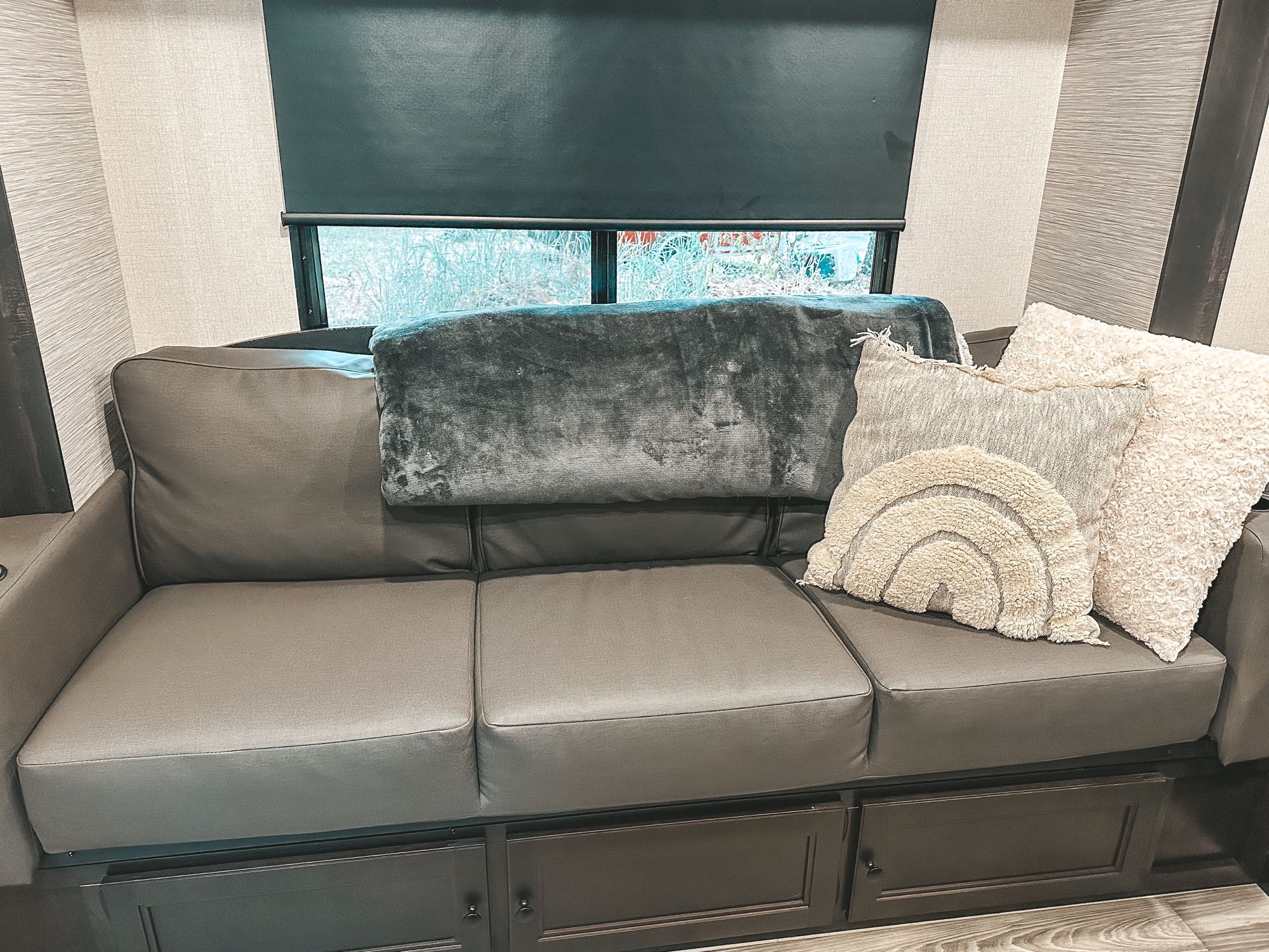 RV rental interior: comfy gray sofa with storage, throw pillows, and a window with a dark roller blind showing foliage.. Starcraft Super Lite Maxx 2022