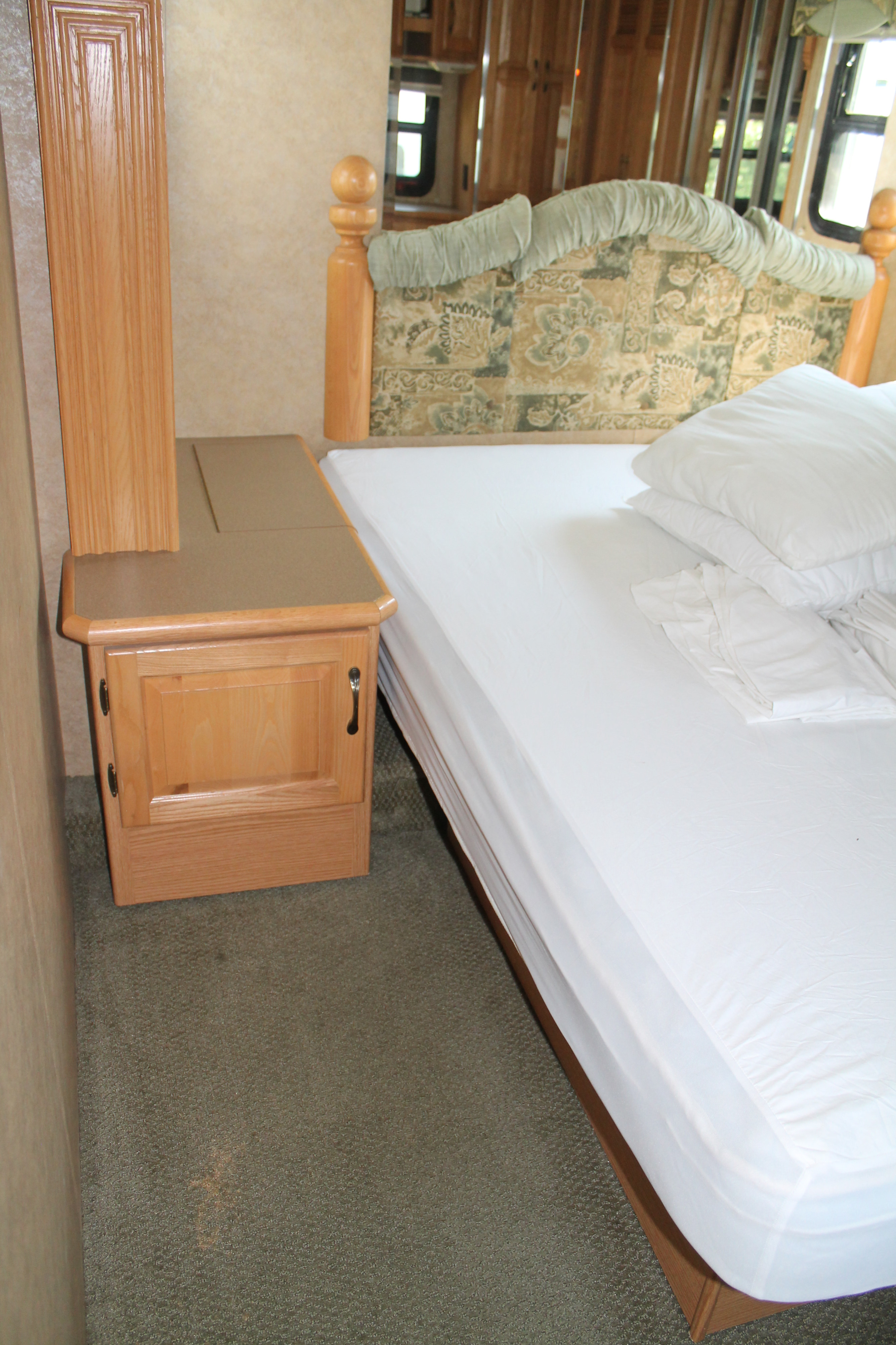 Comfortable RV rental bedroom with a neatly made bed, wooden nightstand, and patterned headboard, ideal for relaxation.. Newmar Cypress 33 RSLH 2007