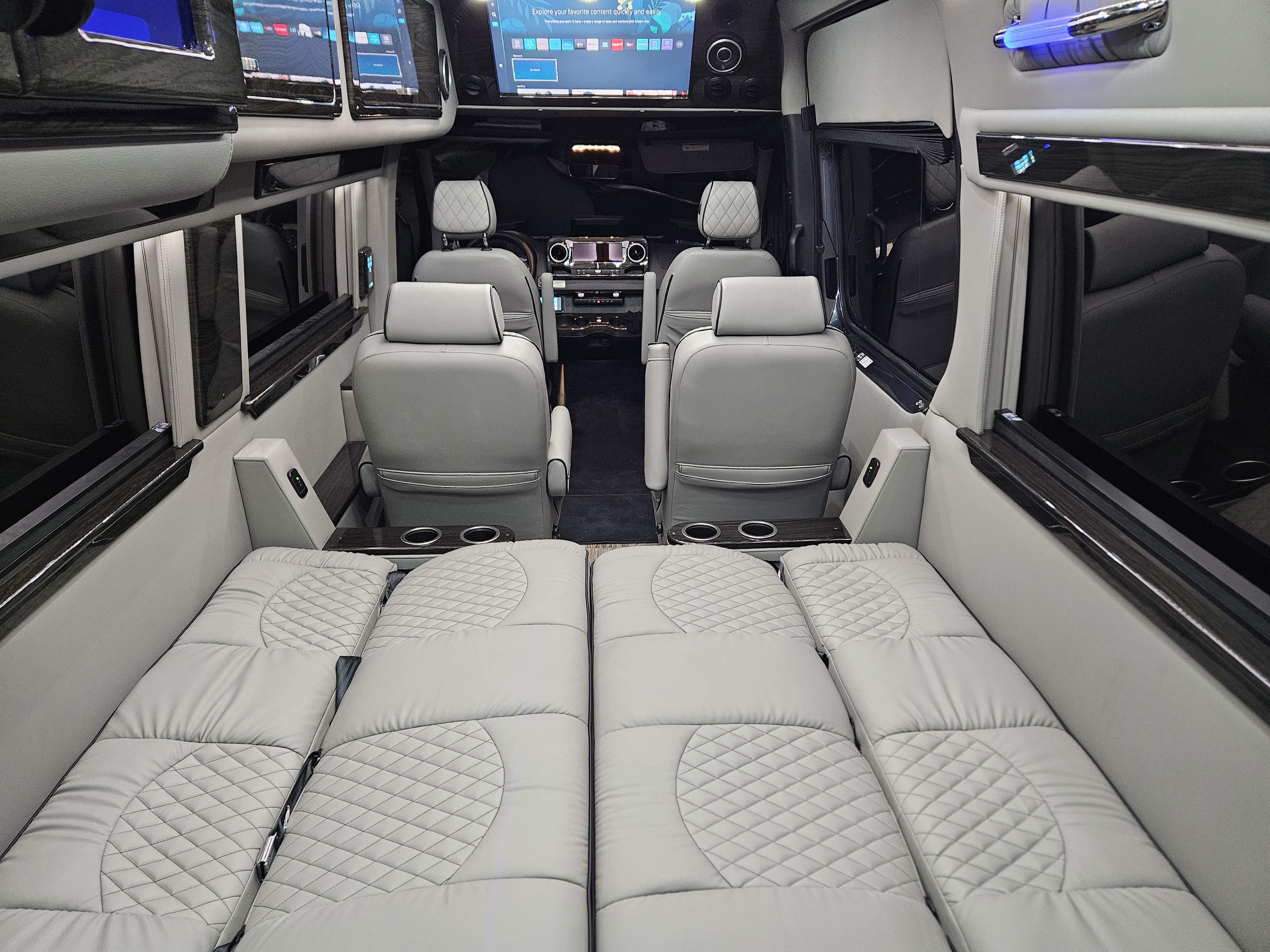 Luxury van RV rental interior: Light gray quilted seating converts to a bed, with screens and cup holders.. Ultimate Toys SPRINTER 2025