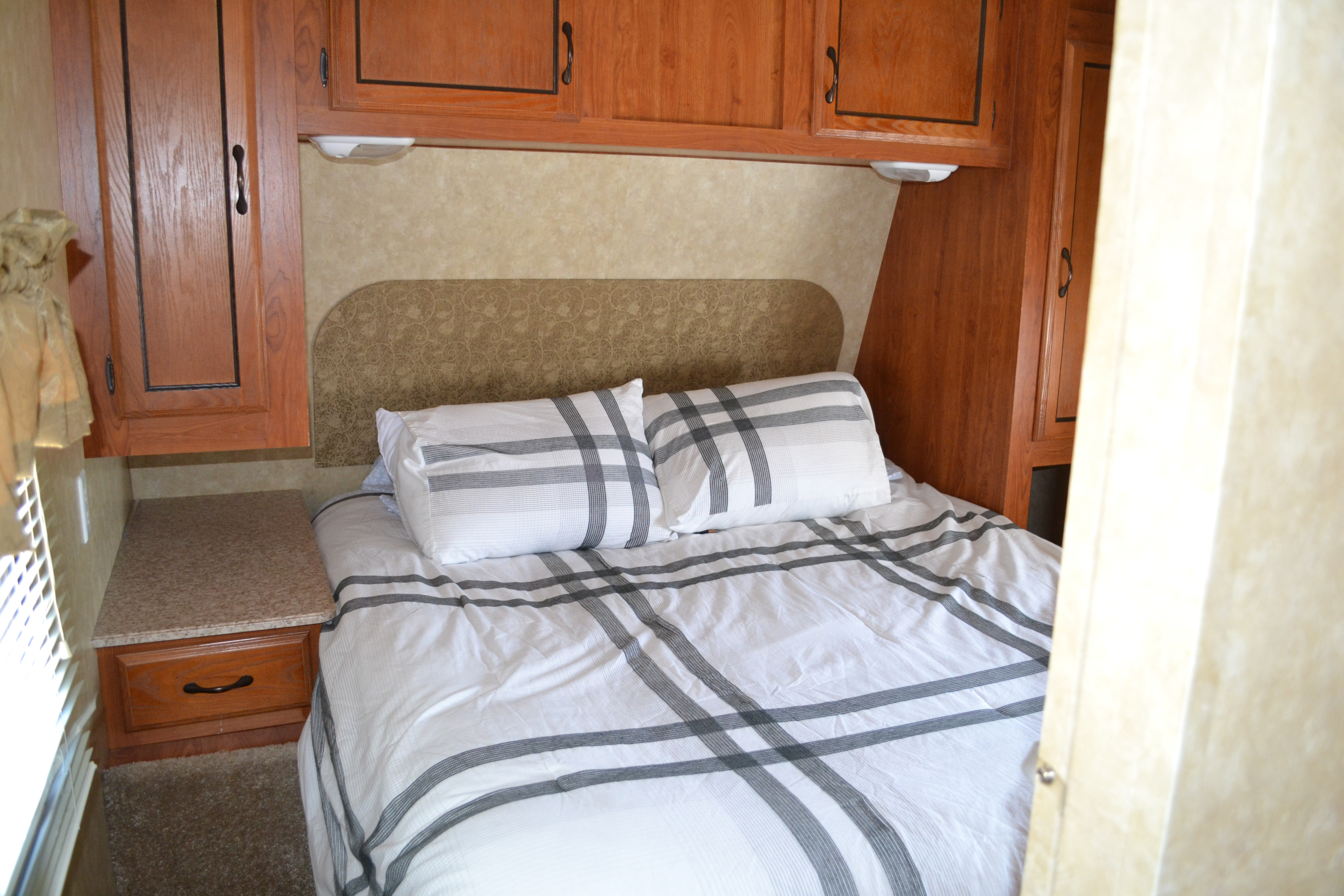 Cozy RV rental bedroom with white and grey striped bedding, wood cabinets, and built-in nightstands.. Forest River Other 2012