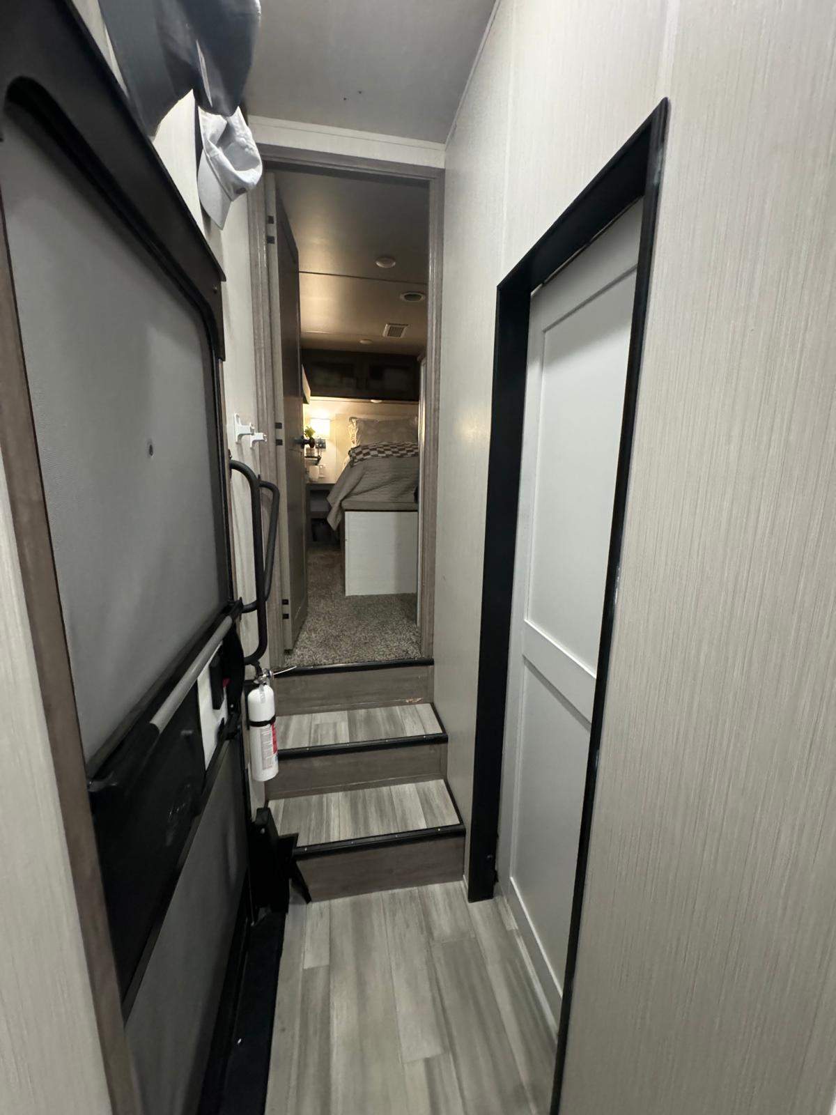 Inside an rv rental: A compact hallway with stairs leads to a cozy bedroom. Note the fire extinguisher by the door for safety.. Cedar Creek Cedar Creek Fifth Wheel 2022