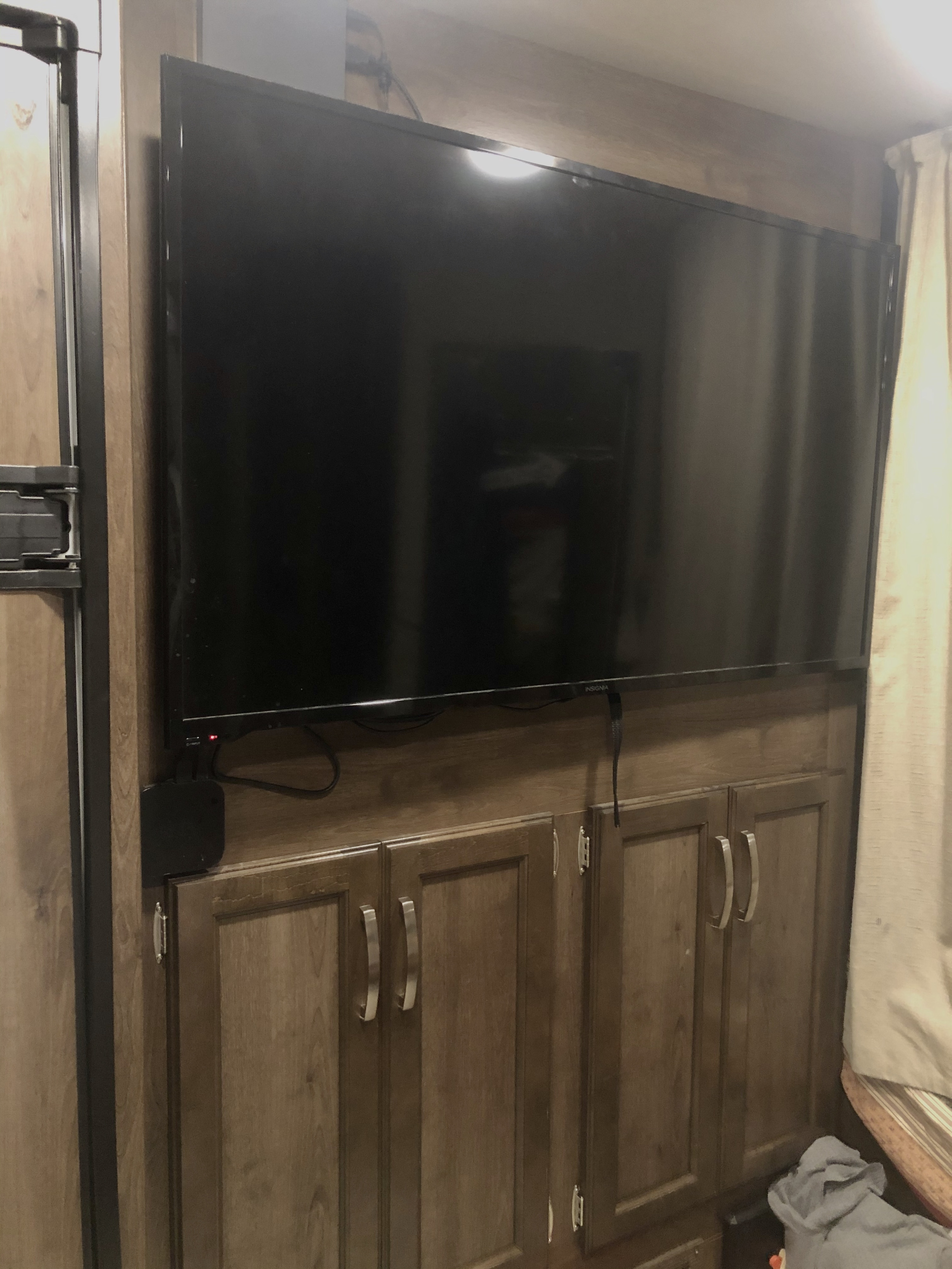 RV rental entertainment setup: a flat-screen TV above wooden cabinets, next to a fridge. Compact & functional.. Jayco Redhawk 2019
