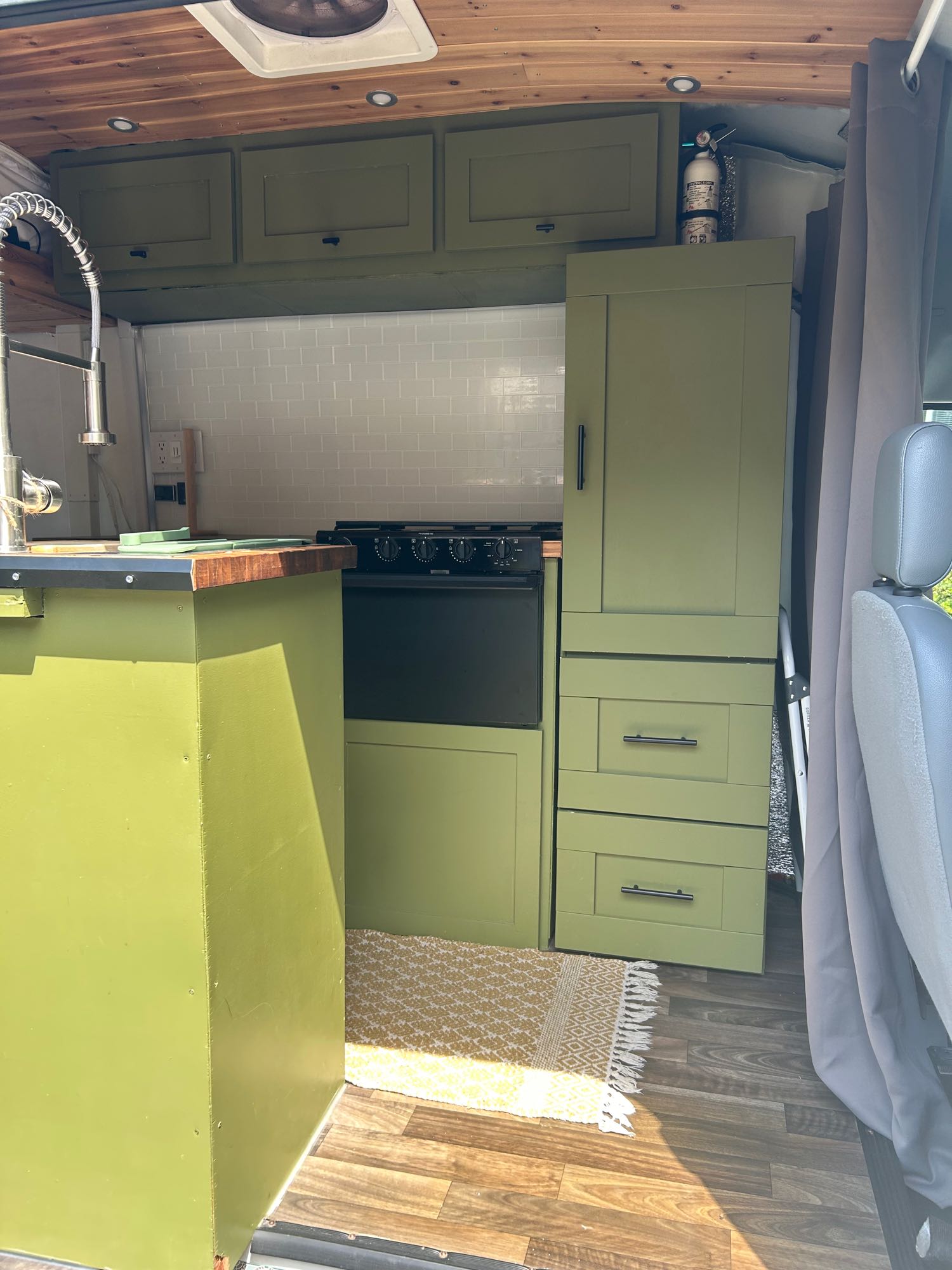 Inside a functional RV rental: green kitchen cabinets, built-in stove, sink, & wood-paneled ceiling for comfort.. Ford Transit 2019