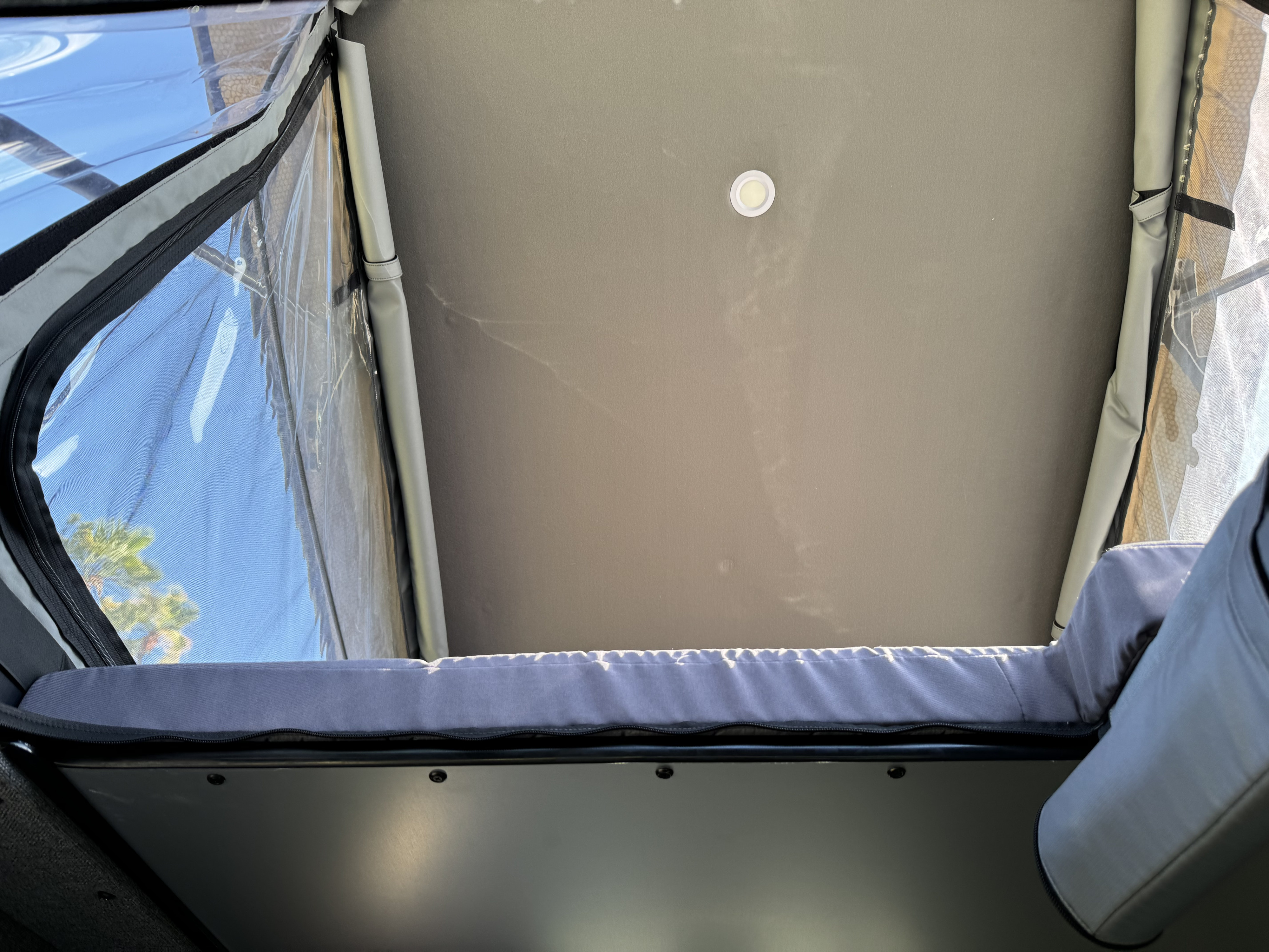 RV rental interior: Looking up into a pop-top tent, showing a comfortable bed, ceiling light, and clear window with sky view.. ModVans ModVans Class B 2023