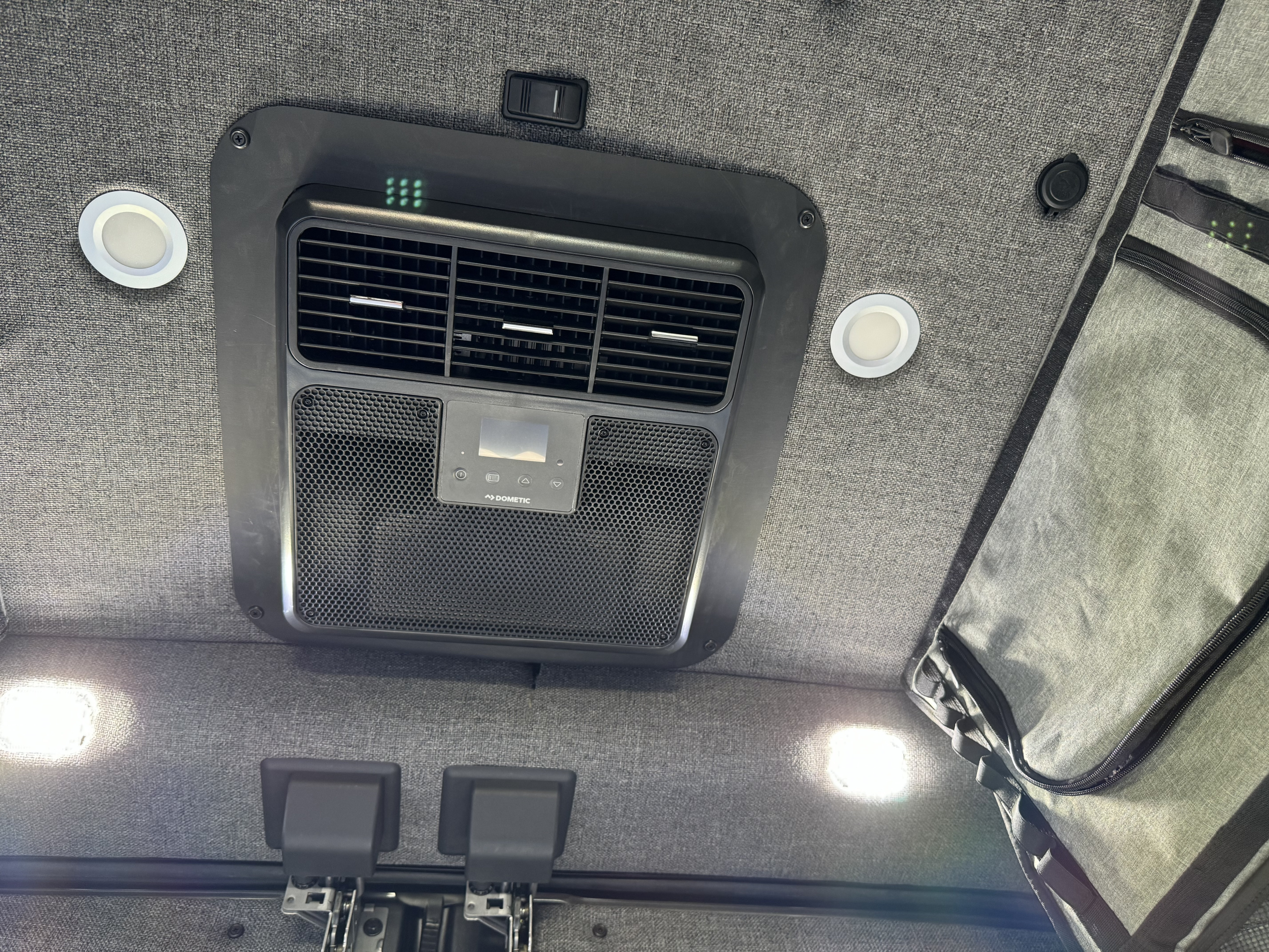 RV rental ceiling: Dometic AC unit, bright LED lights, switch, and hanging storage against a grey fabric backdrop.. ModVans ModVans Class B 2023