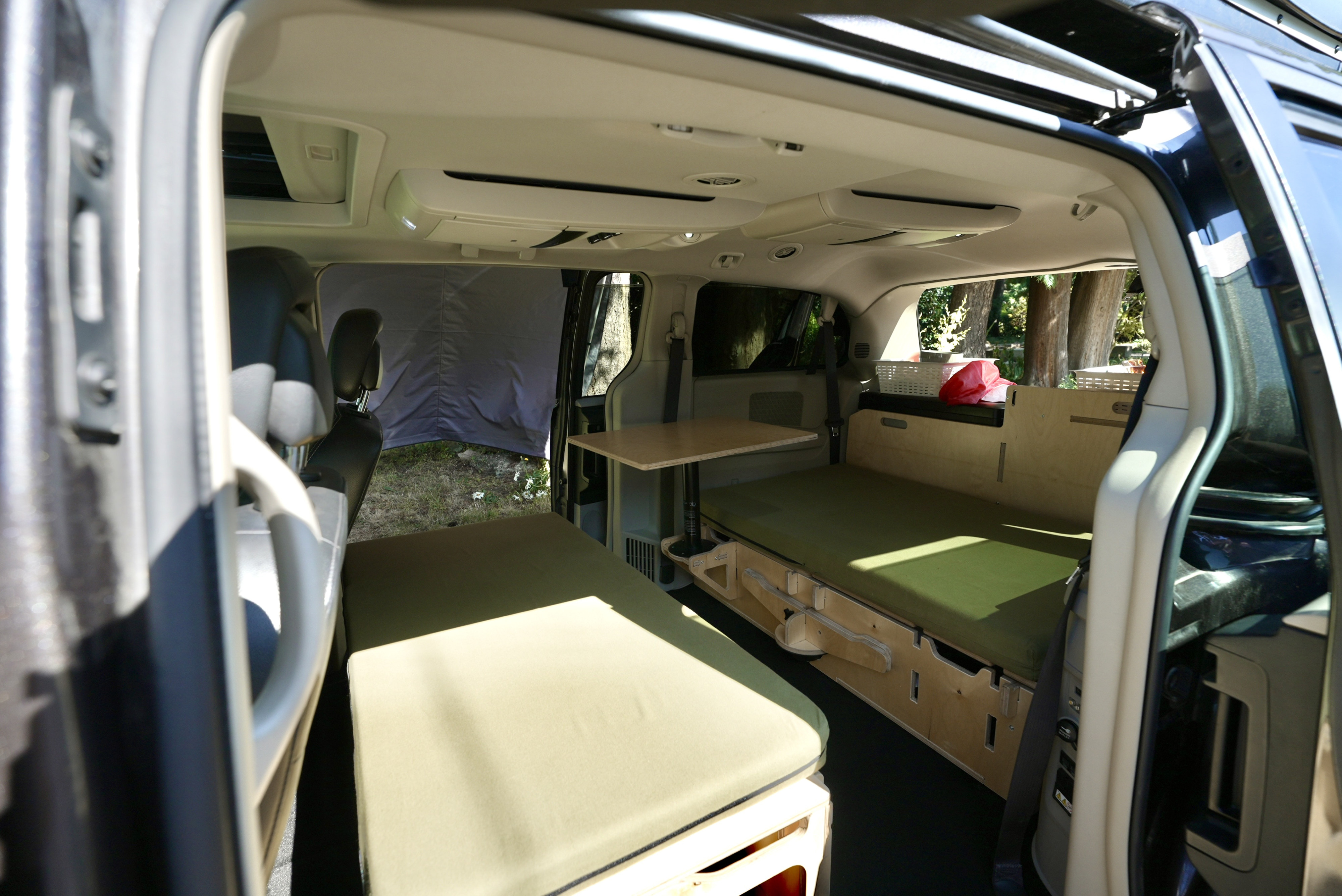 Inside this RV rental, a converted minivan features two bed platforms with green cushions, a wooden table, and storage.. Dodge Caravan 2015