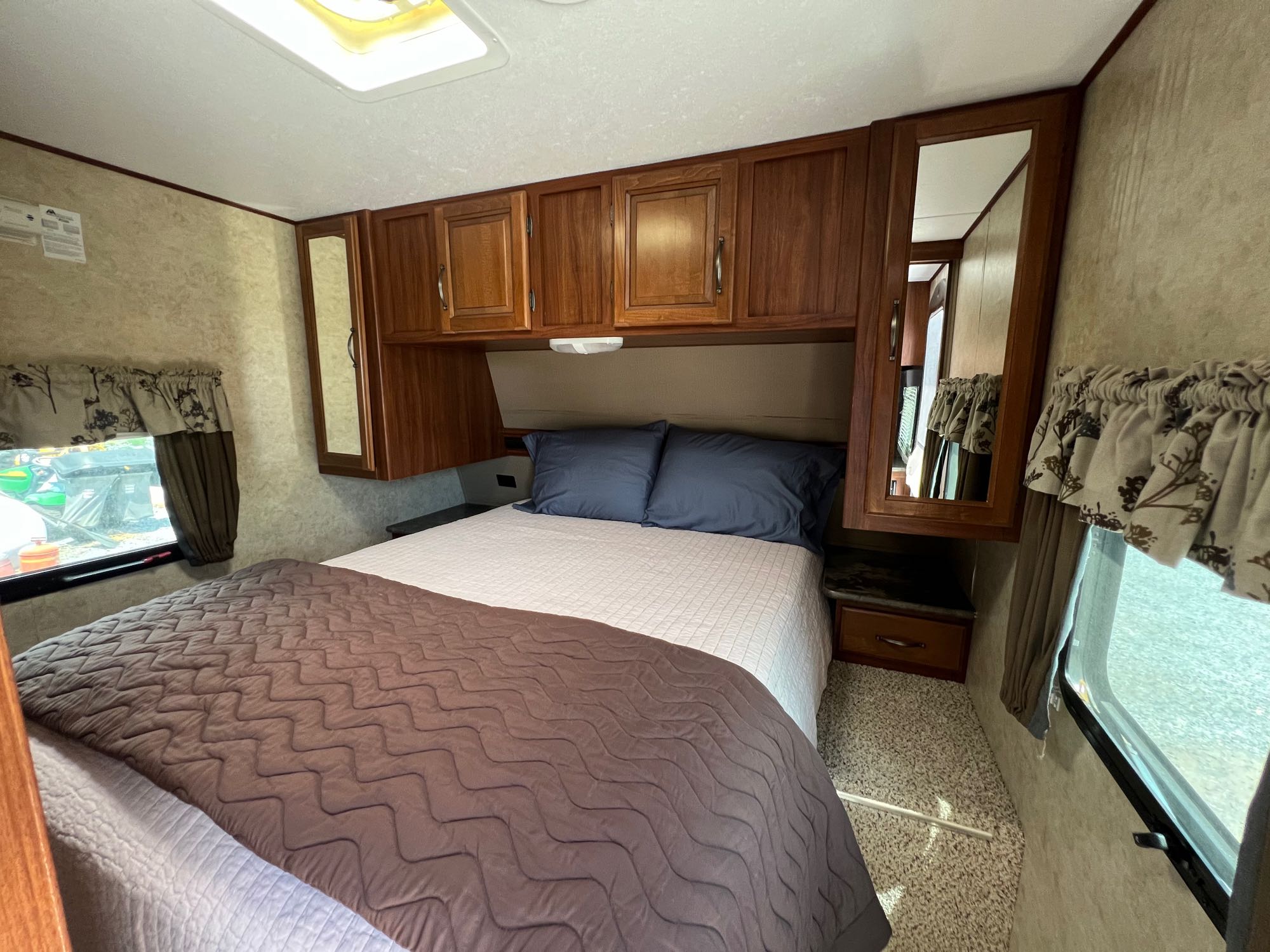 Cozy RV rental bedroom featuring a queen bed, overhead cabinets, mirrors, and windows for a comfortable stay.. Keystone RV Cougar M-31 SQBWE Half-Ton Series 2015