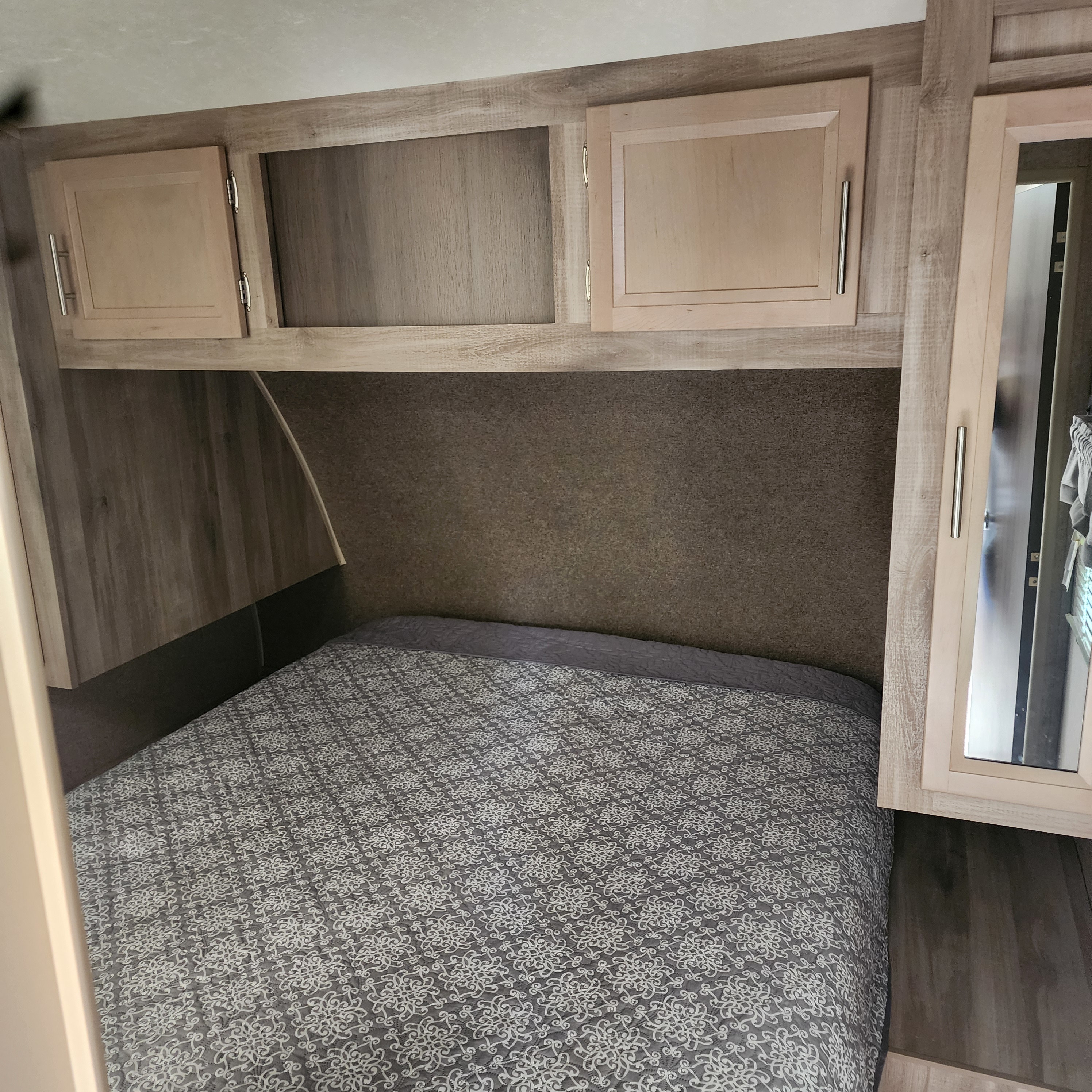 Inside an RV rental, this bedroom features a bed with patterned comforter, wood-toned overhead cabinets, and a mirrored wardrobe.. Forest River Coachmen Catalina Legacy 2019