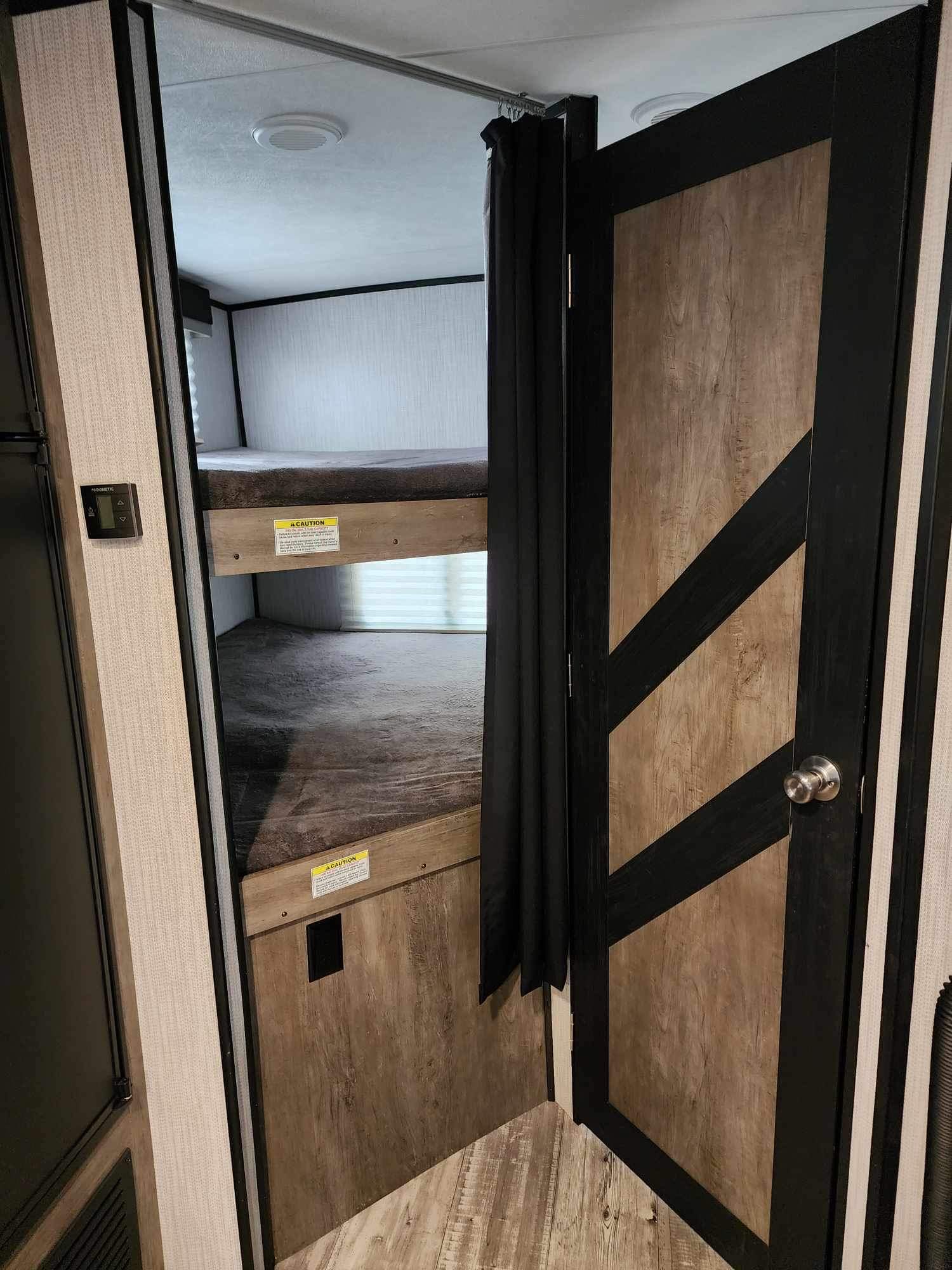 RV rental interior: bunk beds are seen through a stylish, open door. A Dometic control panel is on the left.. Heartland RVs North Trail 2021