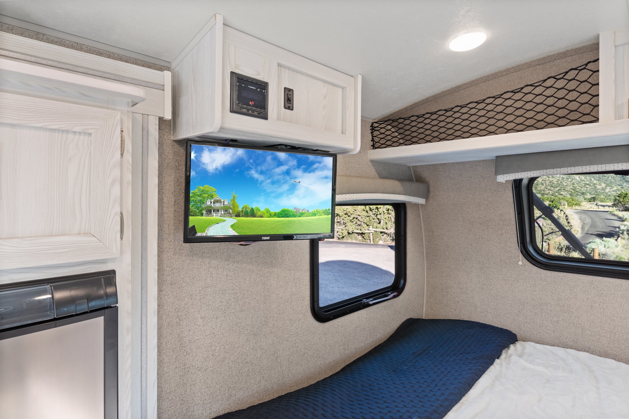Compact RV rental interior showcasing a mounted TV, overhead storage, and a cozy bed, perfect for travel.. Rockwood G19QB 2021