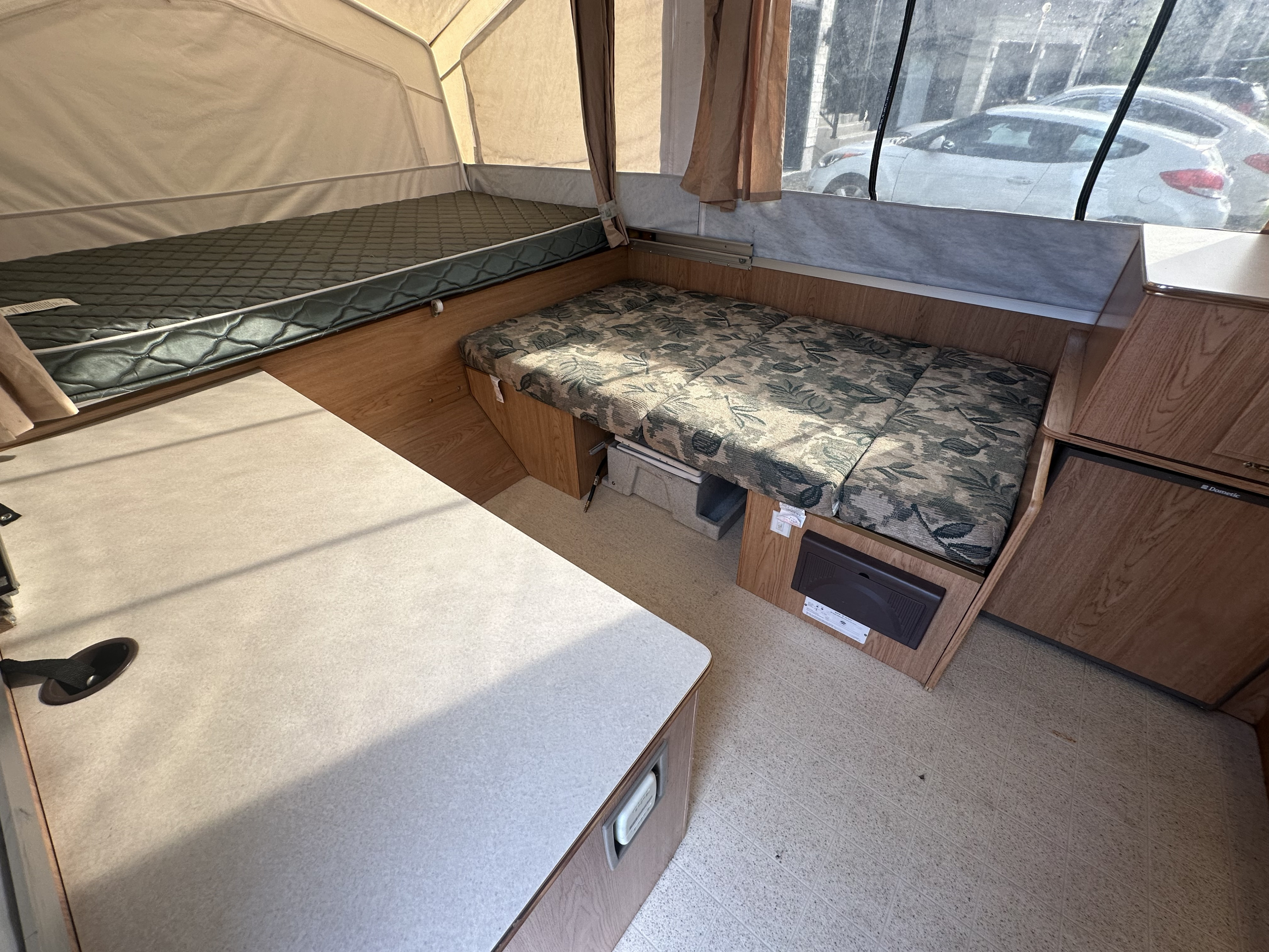 Pop-up camper RV rental interior: two beds, dining table, fridge & cabinets. View out window shows a car.. Forest River Rockwood LTD 2005