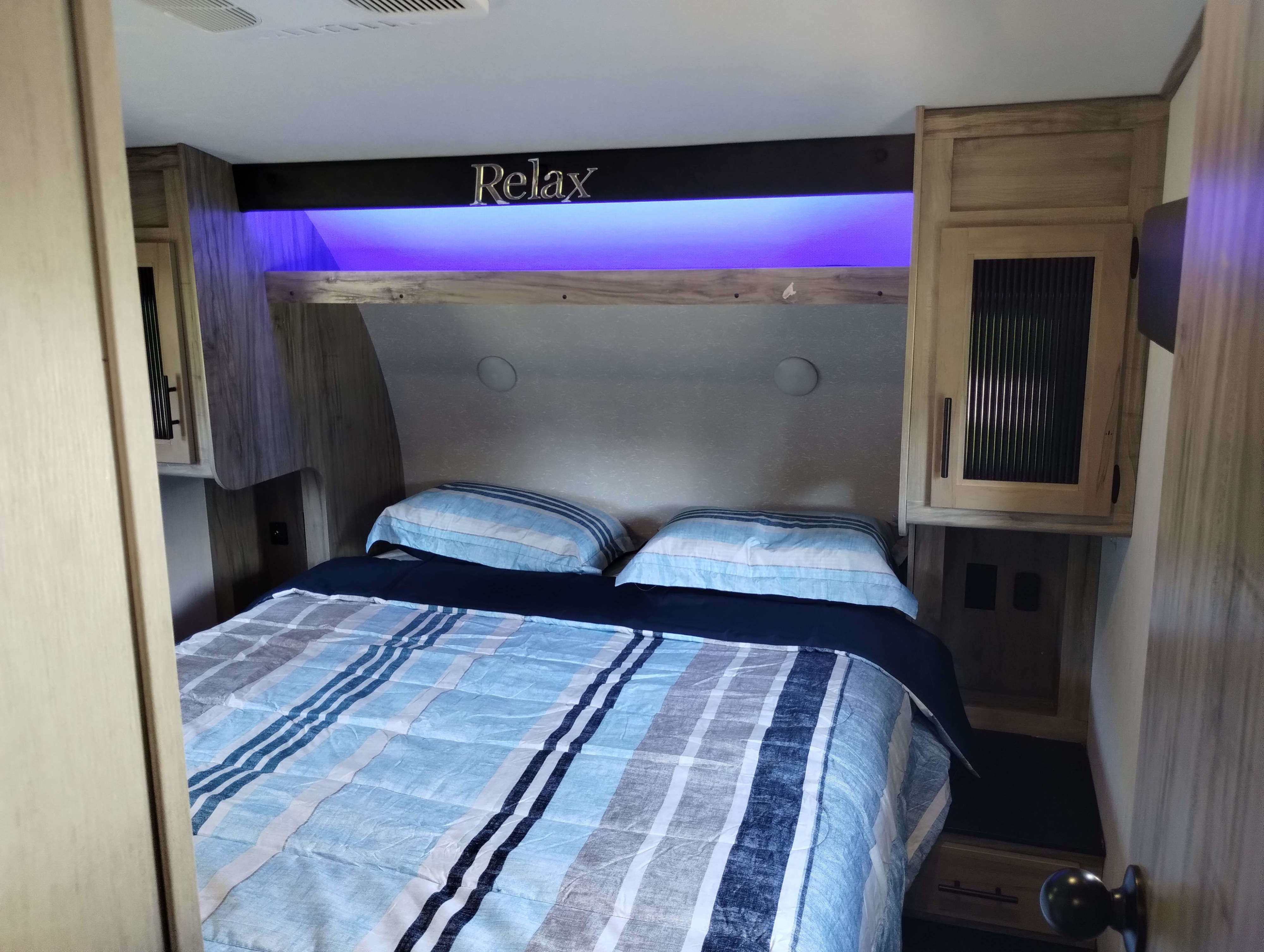Cozy RV rental bedroom with striped bedding, ambient blue light, and a "Relax" sign above the bed.. Forest River Cherokee Arctic Wolf 2021