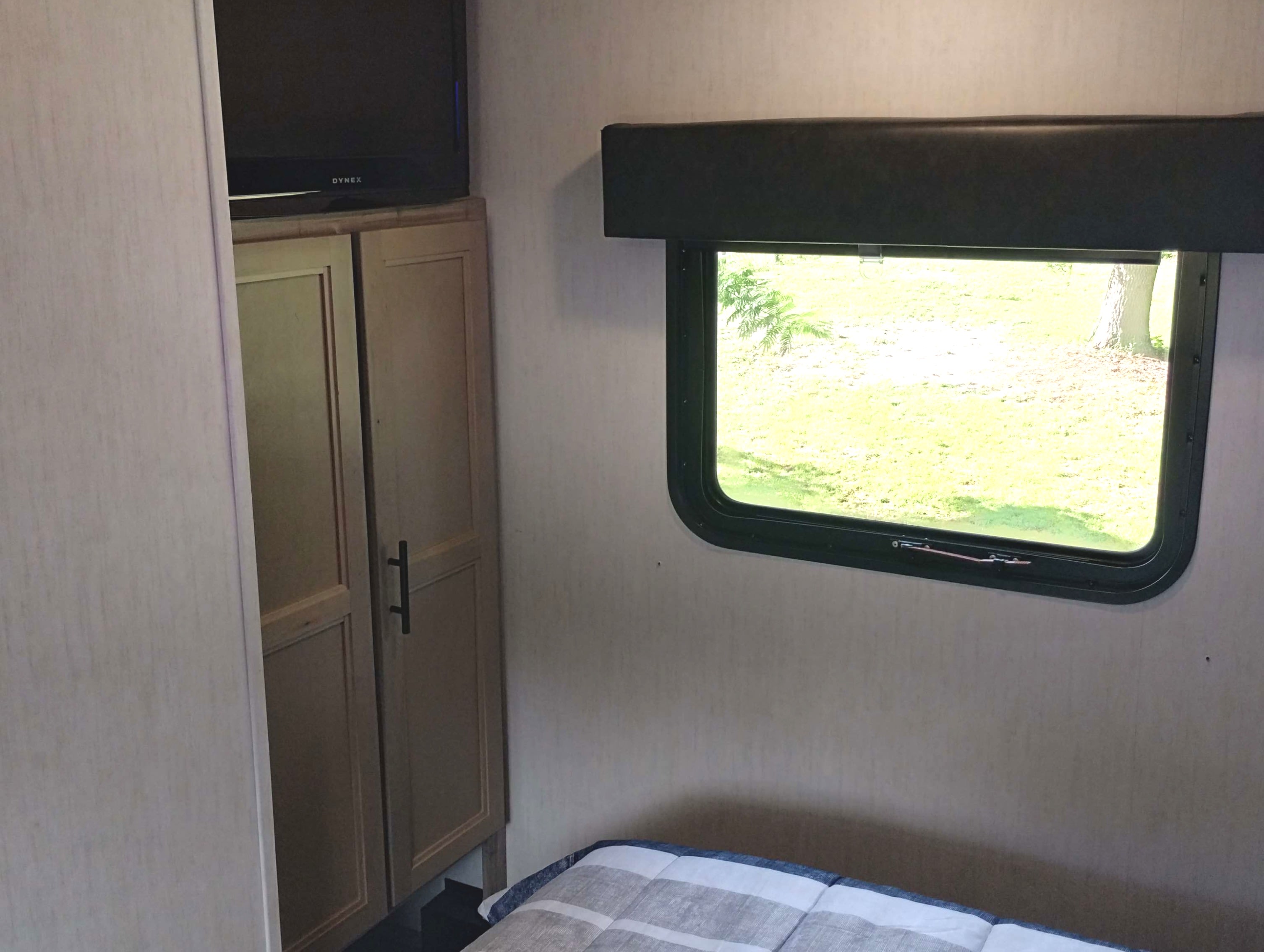 Inside an RV rental bedroom, featuring a window with an outdoor view, a bed, TV, and wardrobe.. Forest River Cherokee Arctic Wolf 2021