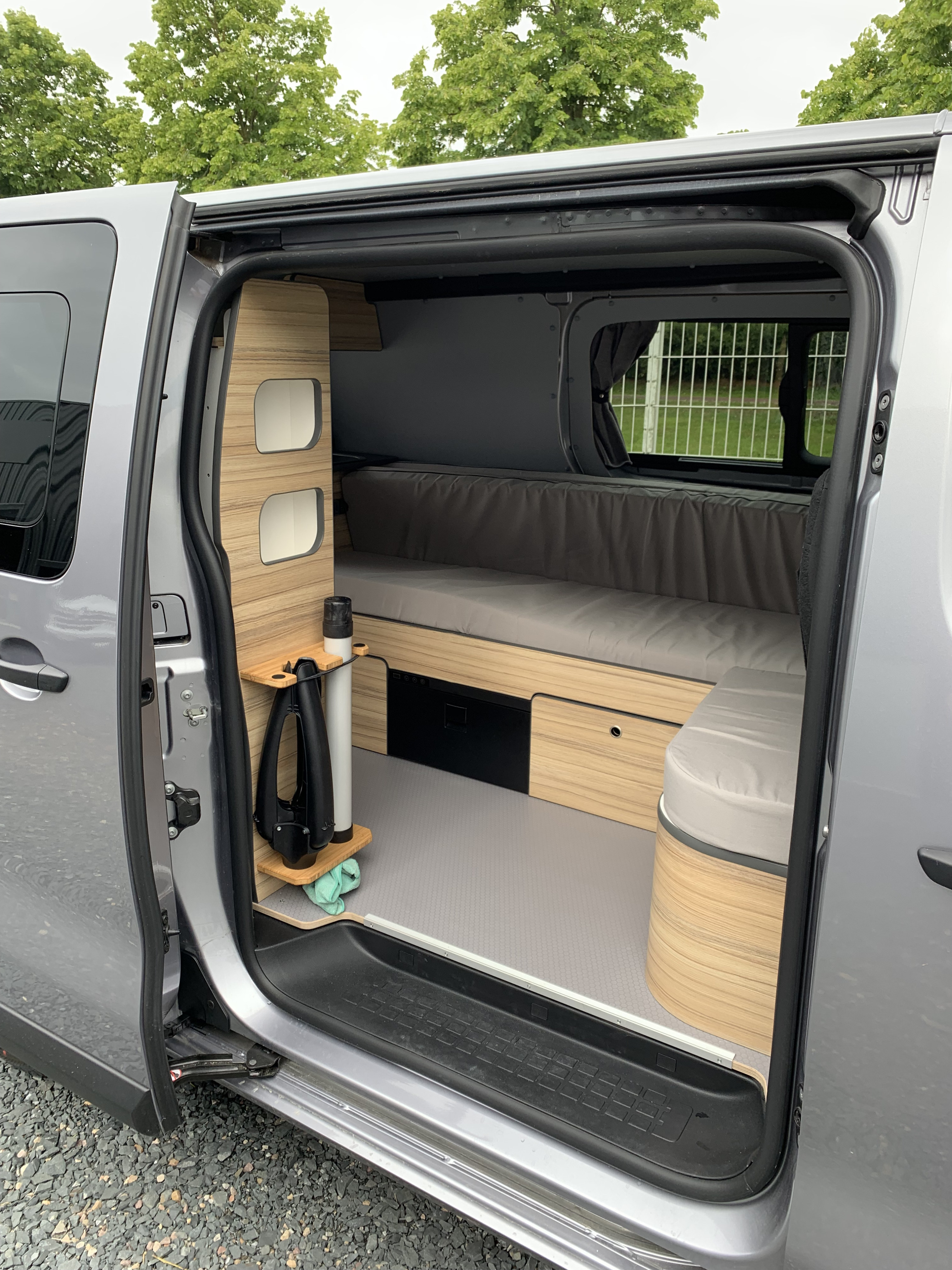 Step inside this RV rental! Compact camper van interior with wood cabinetry, comfortable bed, storage, and integrated fridge.. opel L'OTAGO (Caen) 2024