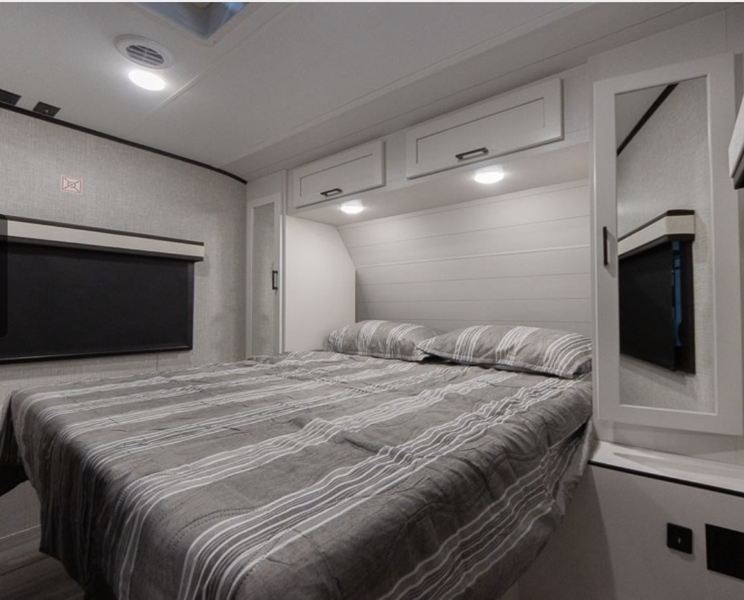 Clean, modern RV rental bedroom with a striped bed, shiplap headboard, and overhead storage. Well-lit and cozy.. Jayco Jay Feather 2024