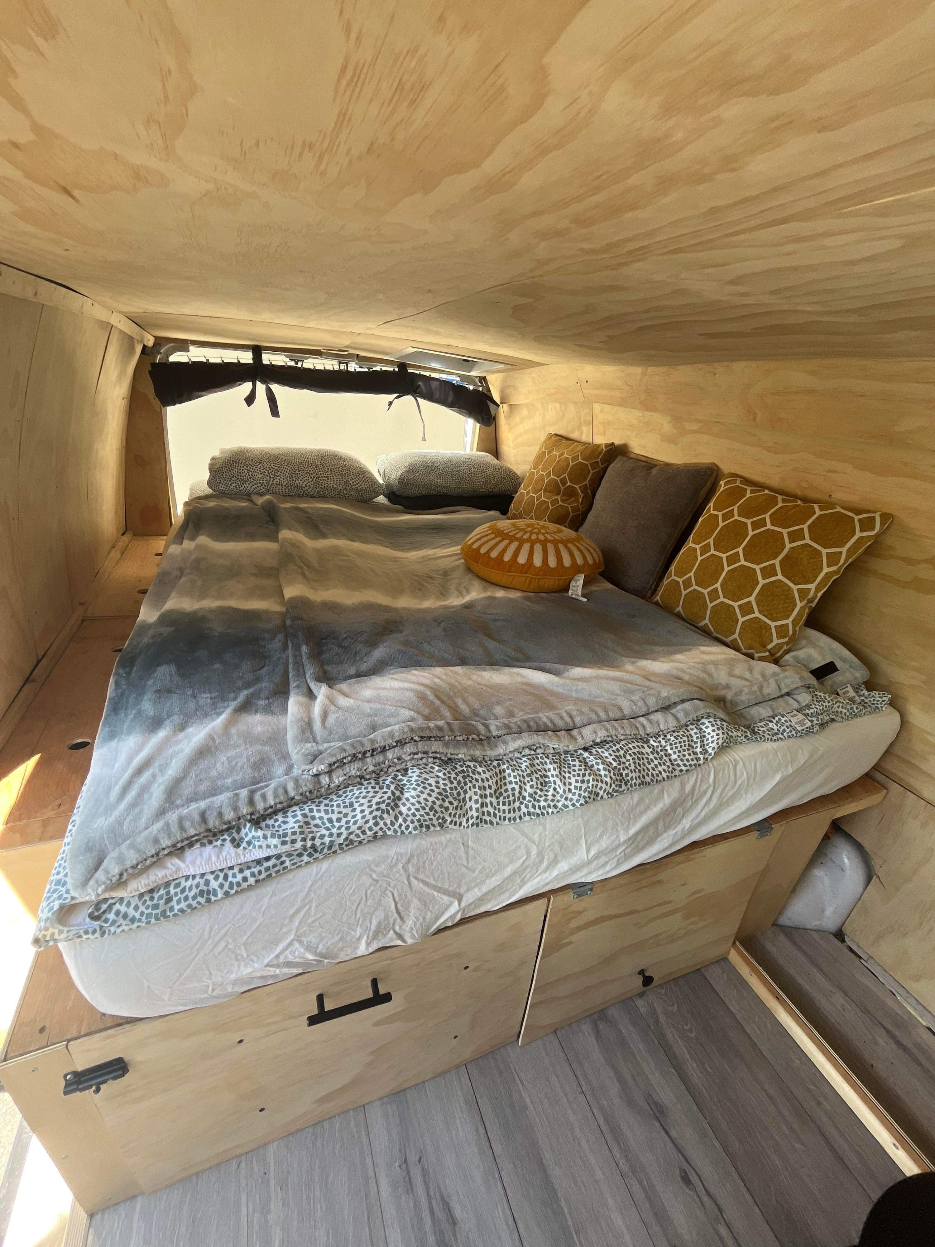 Cozy wood-paneled RV rental interior with a comfy bed, striped blanket, colorful pillows, and under-bed storage.. Ford Econolline 250s 2003